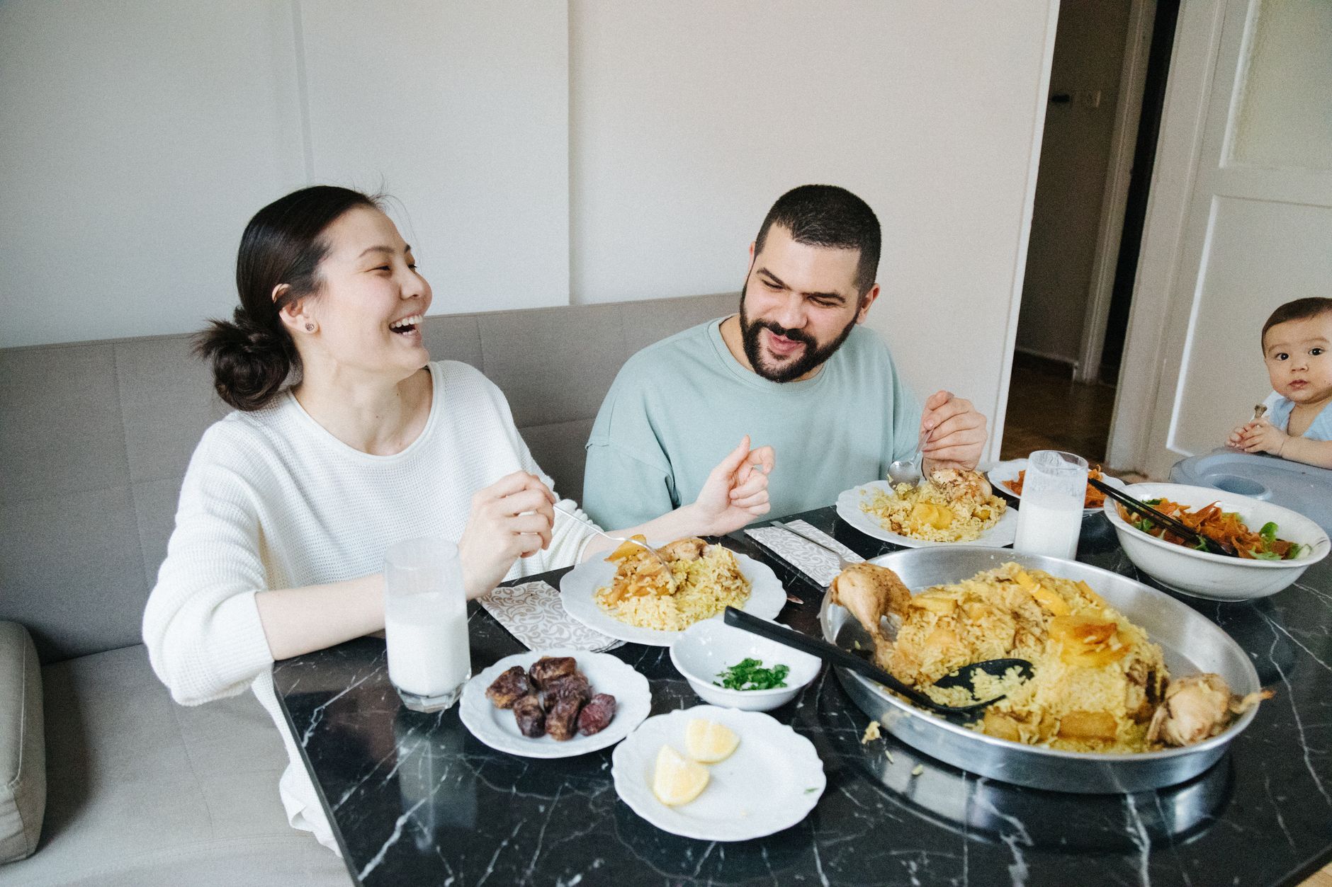A smiling couple enjoys a meal at home with their baby, celebrating family togetherness.