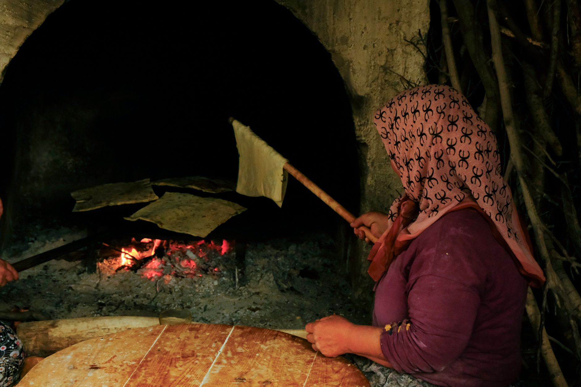 زنی نان سنتی را روی آتش باز در آشپزخانه‌ای روستایی می‌پزد.