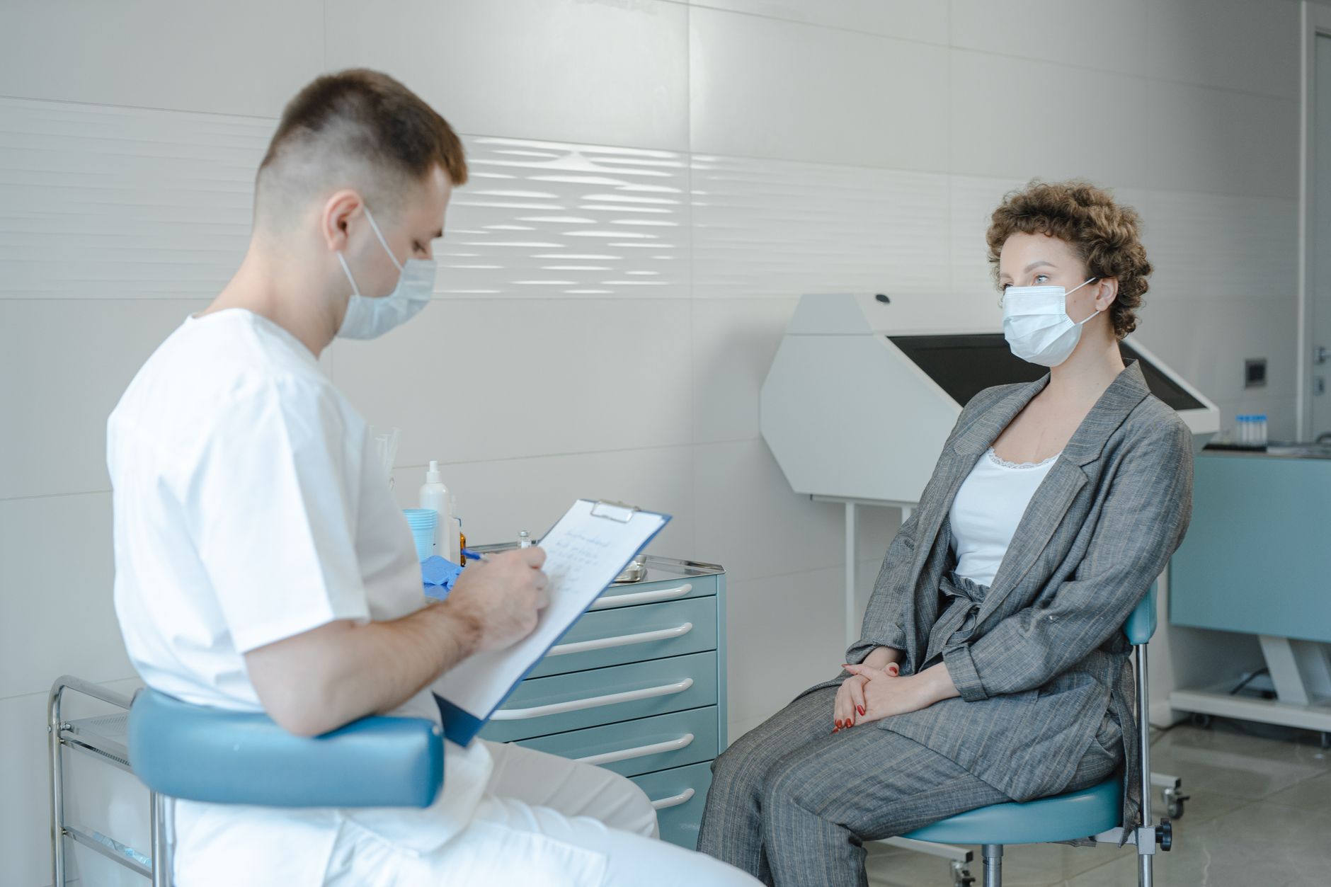 A doctor and patient in masks discuss in a modern Turkish clinic setting.