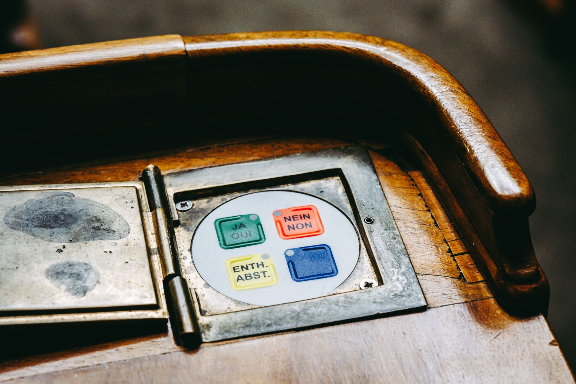 Close-up of multilingual voting buttons labeled JA, NON, and others on a wooden desk.