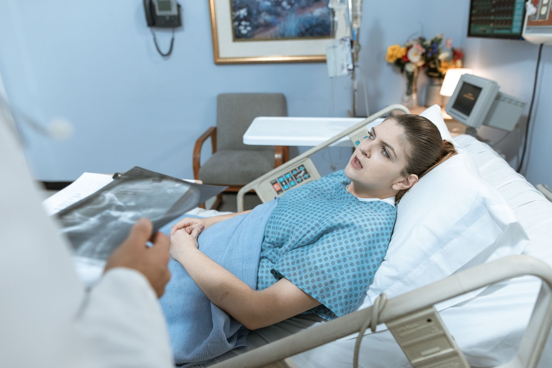 A patient in a hospital bed talks to a healthcare provider, looking concerned.