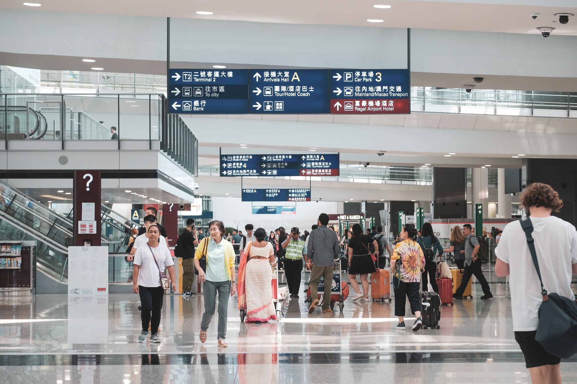 Crowded airport terminal filled with medical tourists carrying luggage, directions visible.