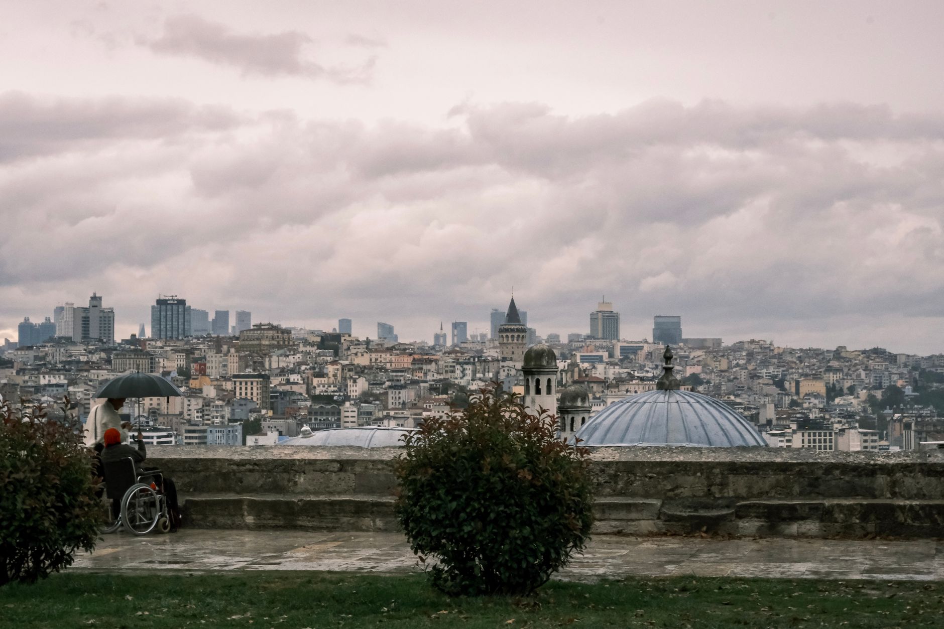 A person with an umbrella overlooks Istanbul's skyline from a hill.