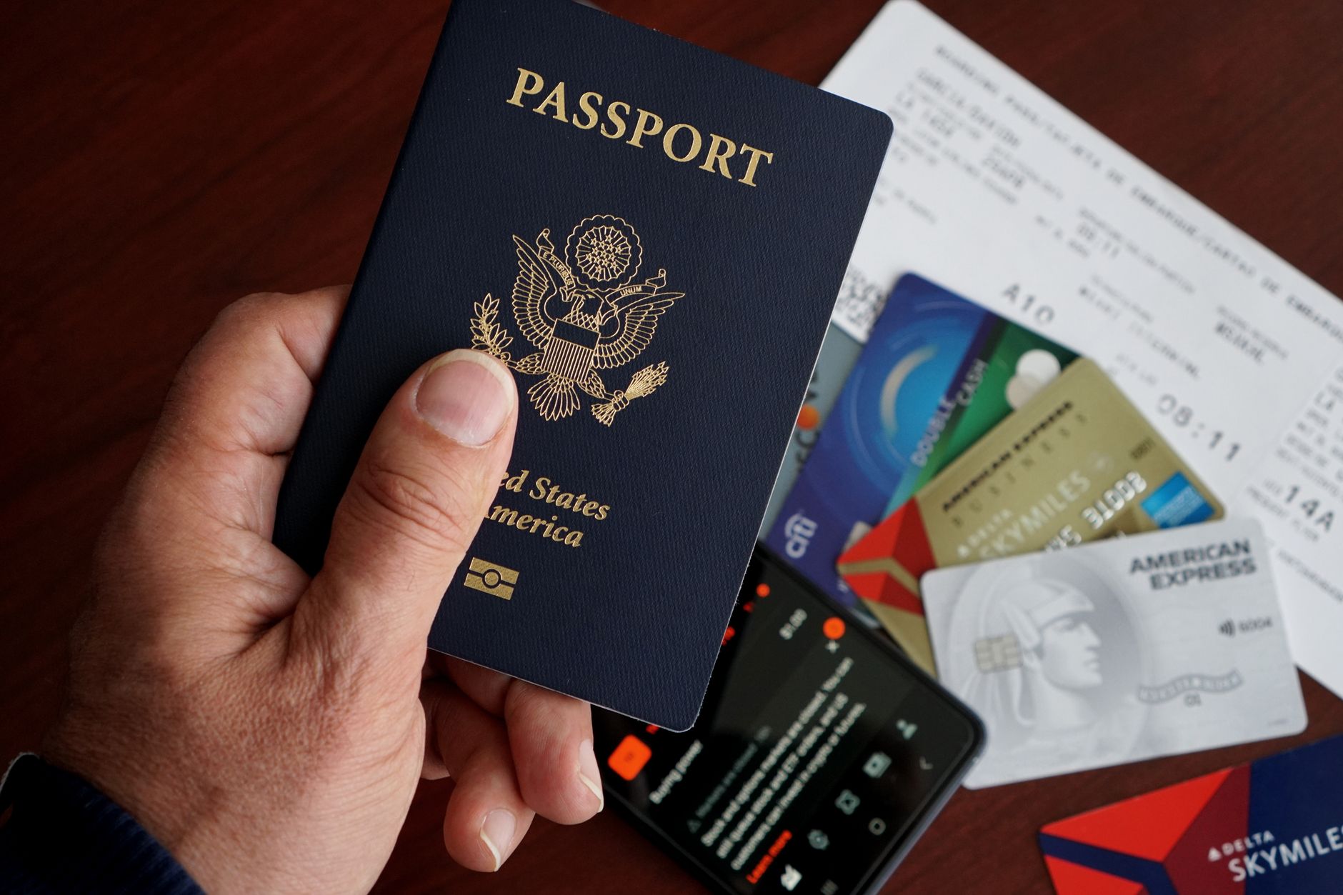 A hand holding a US passport, surrounded by boarding passes and credit cards on a table.