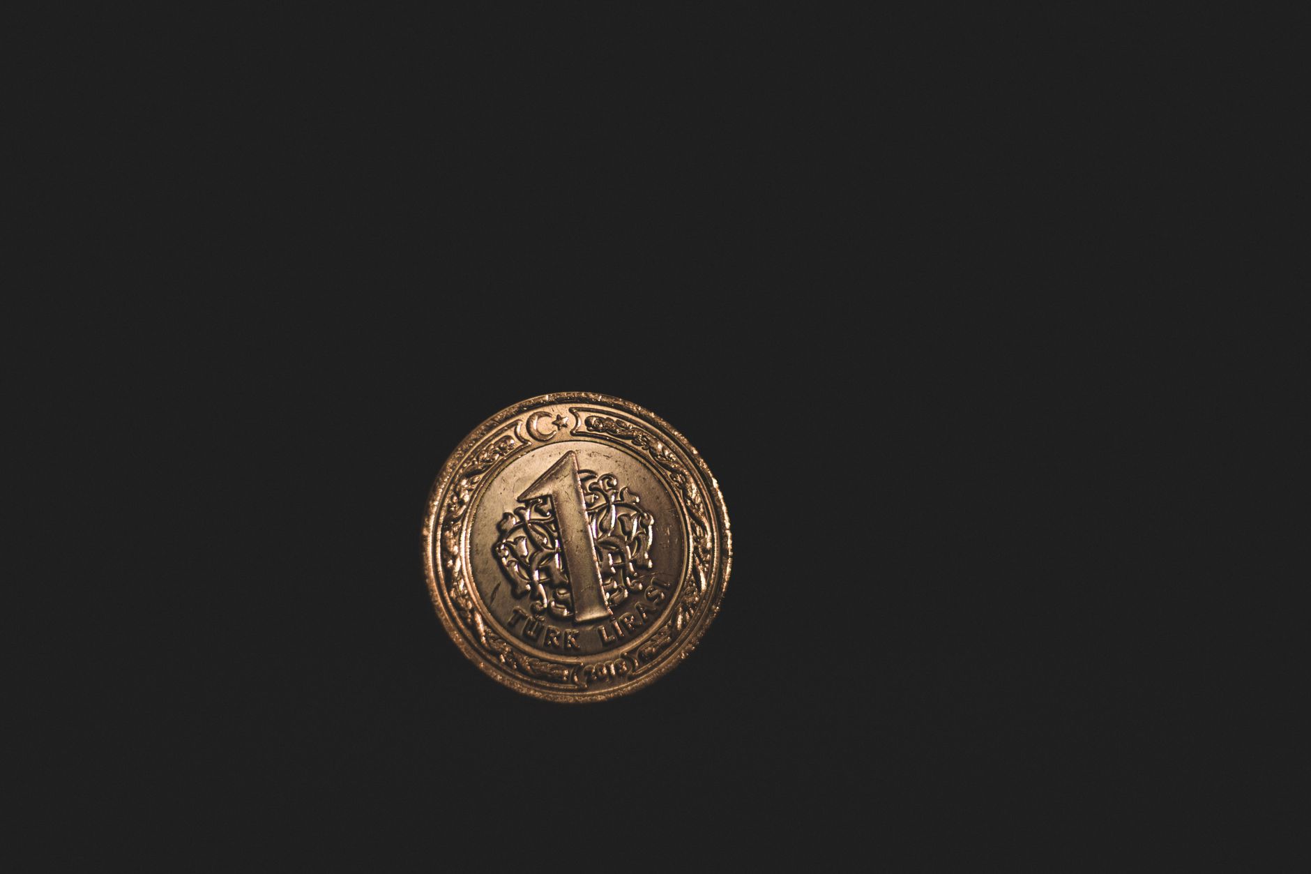 A one Turkish lira coin resting on a black background, symbolizing financial transactions.