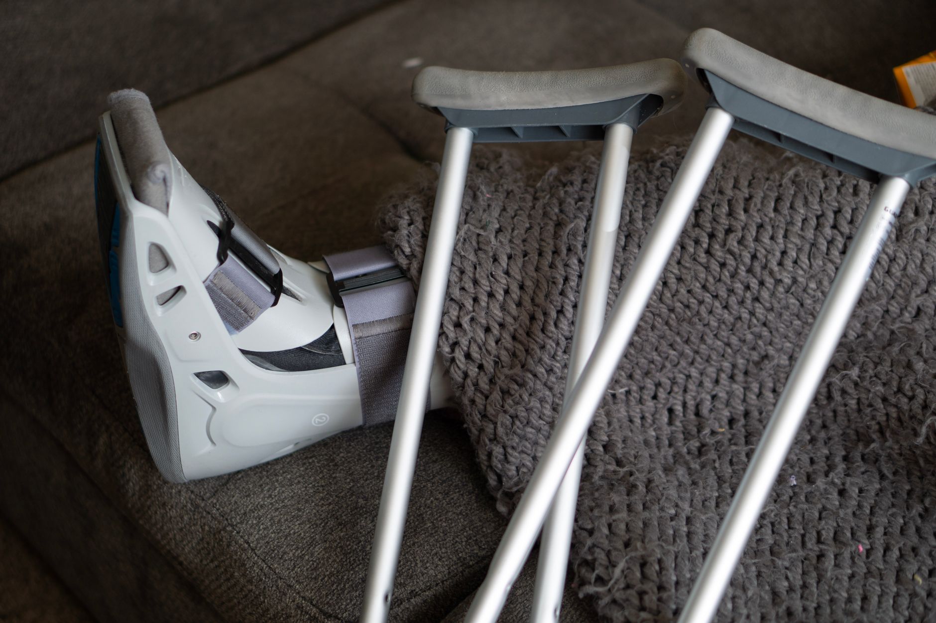 A patient's foot in a walking boot rests on a couch alongside crutches.