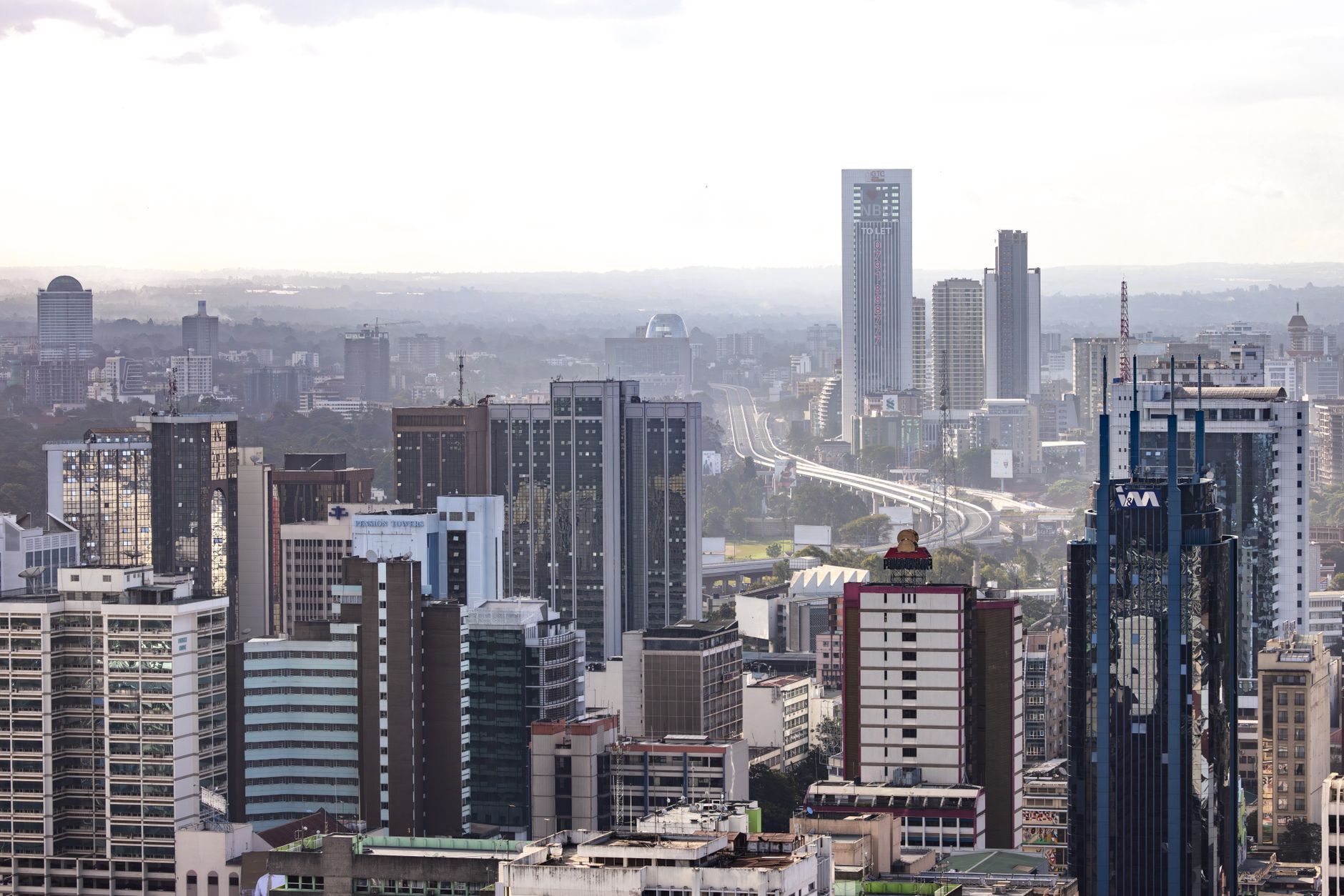 Bulutlu bir gökyüzü altında çeşitli gökdelenler ve otoyollarıyla Nairobi'nin panoramik silüeti.