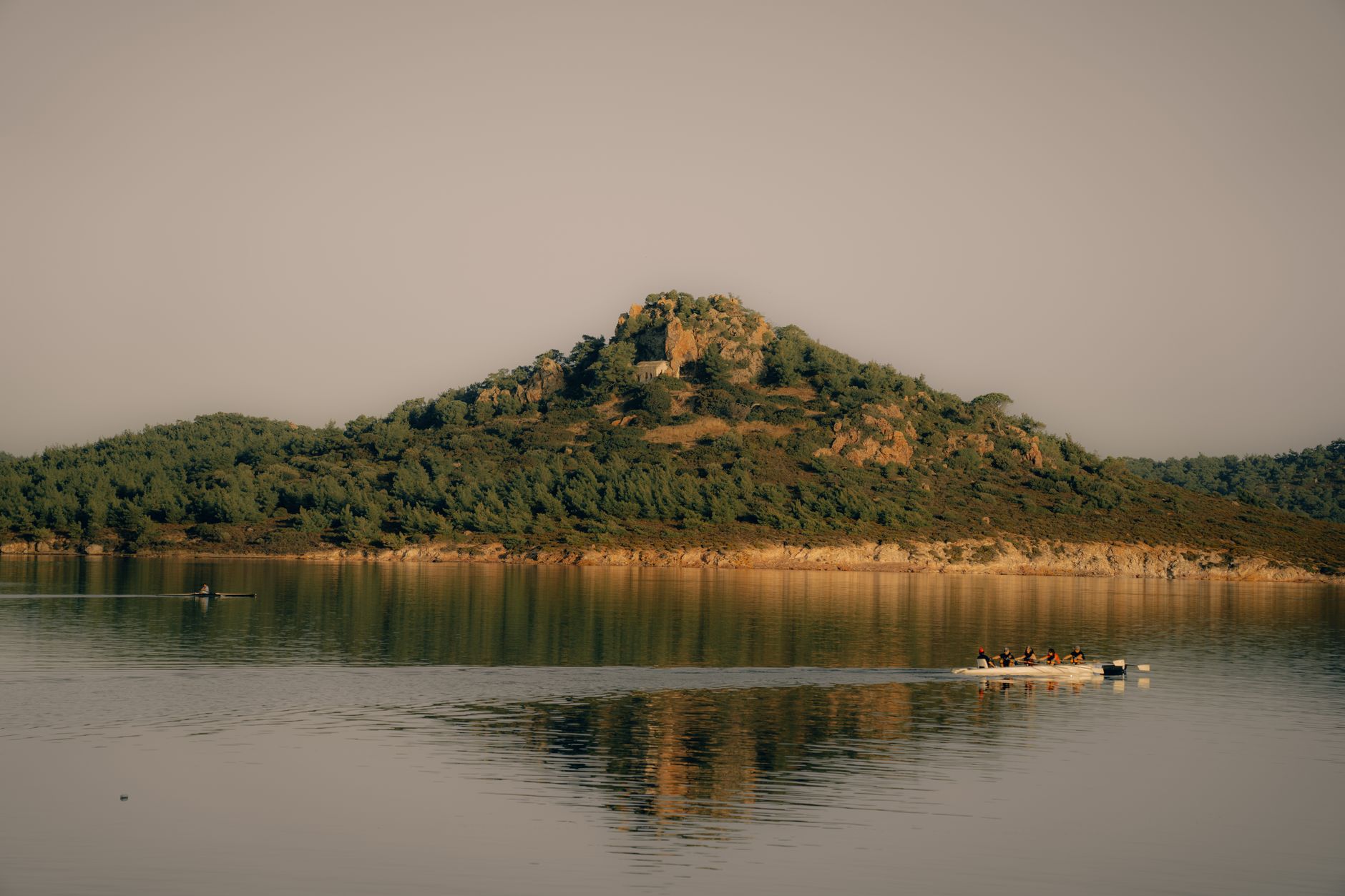 A lone paddler glides across a calm mountain lake in Türkiye, surrounded by misty hills.