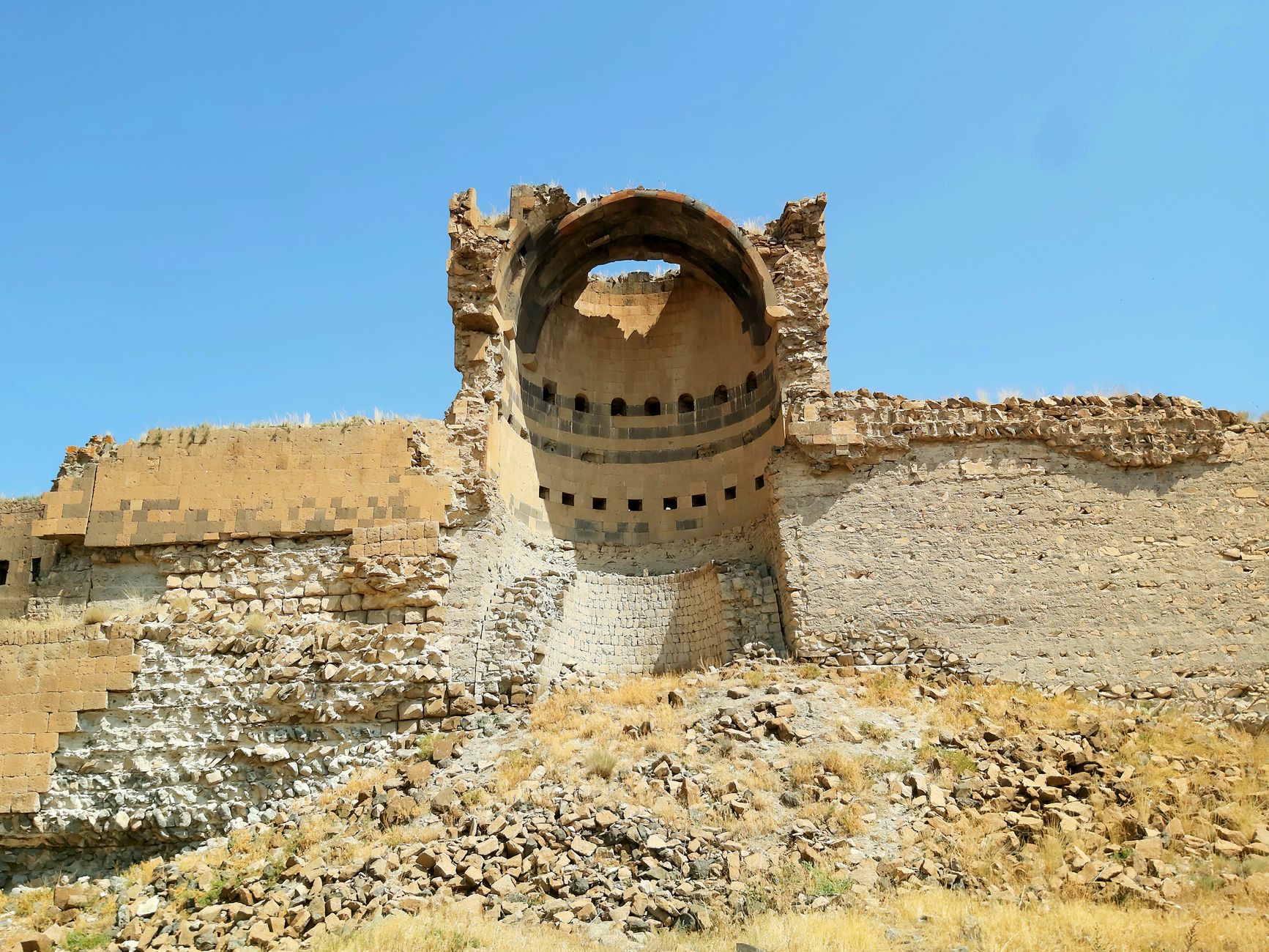The remains of a cathedral with a dome at Ani, showcasing ancient stone walls and grassy surroundings.