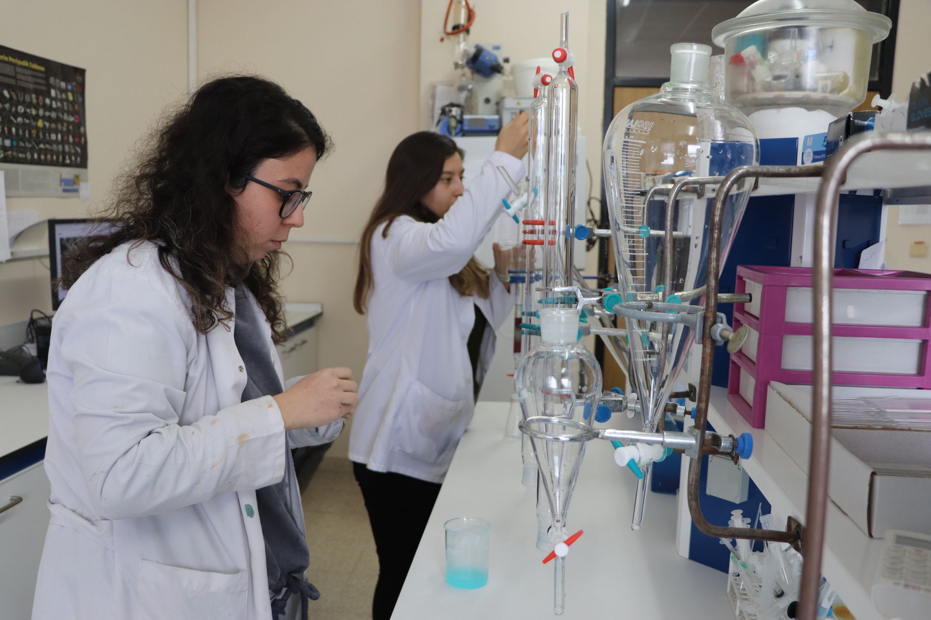 Two women in lab coats working with laboratory equipment to prepare radioactive doses.