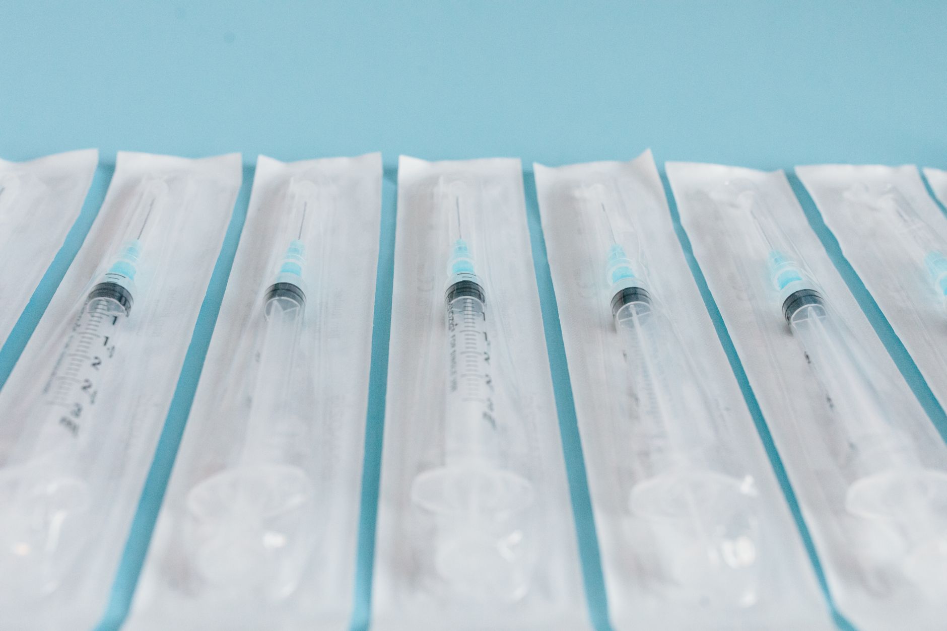 A row of packaged surgical syringes with blue caps against a blue background.