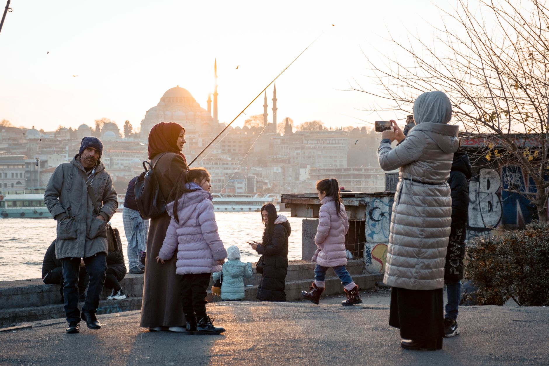 A family captures memories by the Bosphorus at sunset in Istanbul, featuring children and adults by the water.