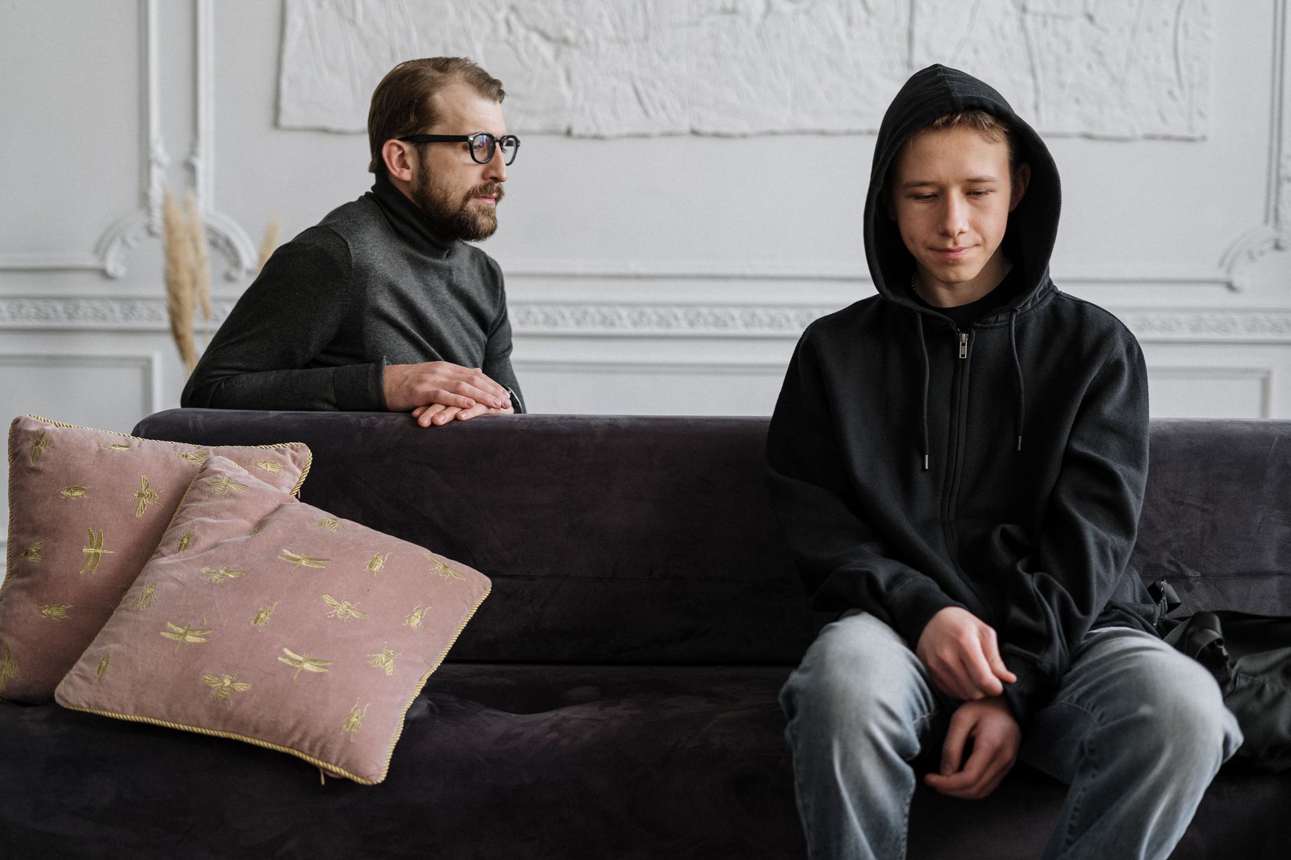 A psychologist and an adolescent sit together in a stylish living room during a family counseling session.