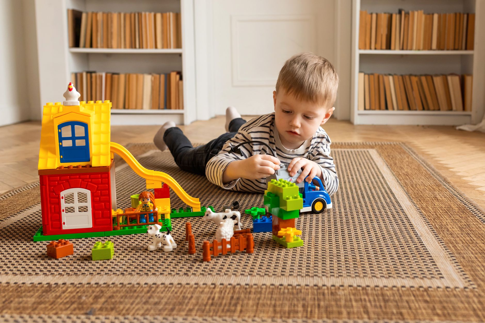 A young child engages in imaginative play with LEGO toys, including a colorful house and animal figures.