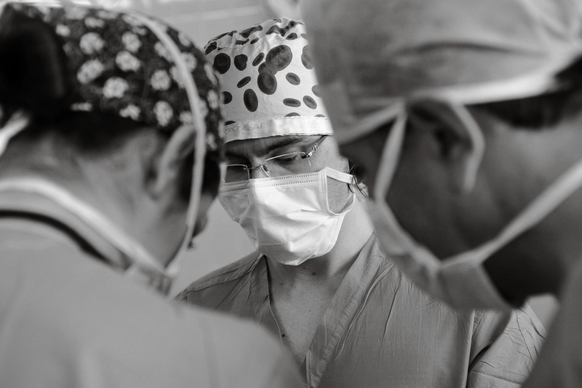 Three surgeons in masks and caps focused on a procedure in black and white.