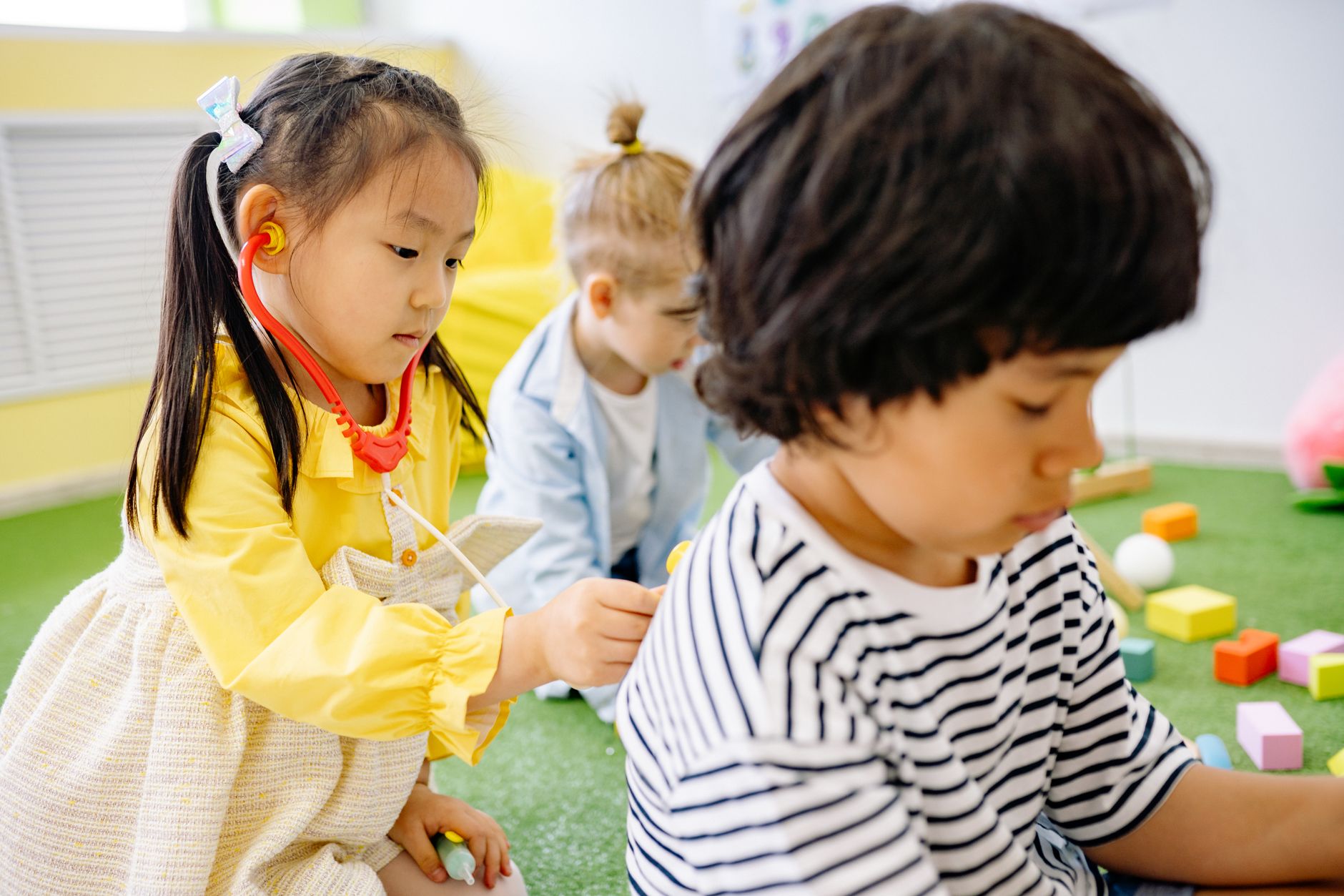 Two children engaged in imaginative play with medical toys in a hospital playroom.