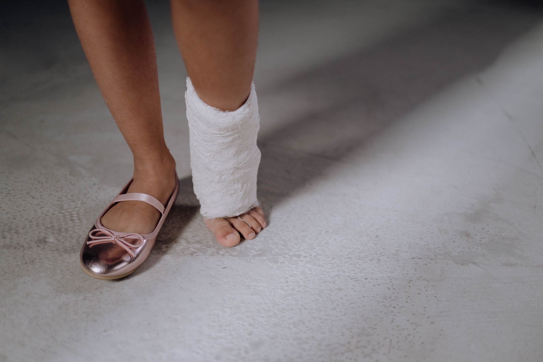 Close-up of a child's foot with a white cast and a pink ballet shoe on a smooth surface.