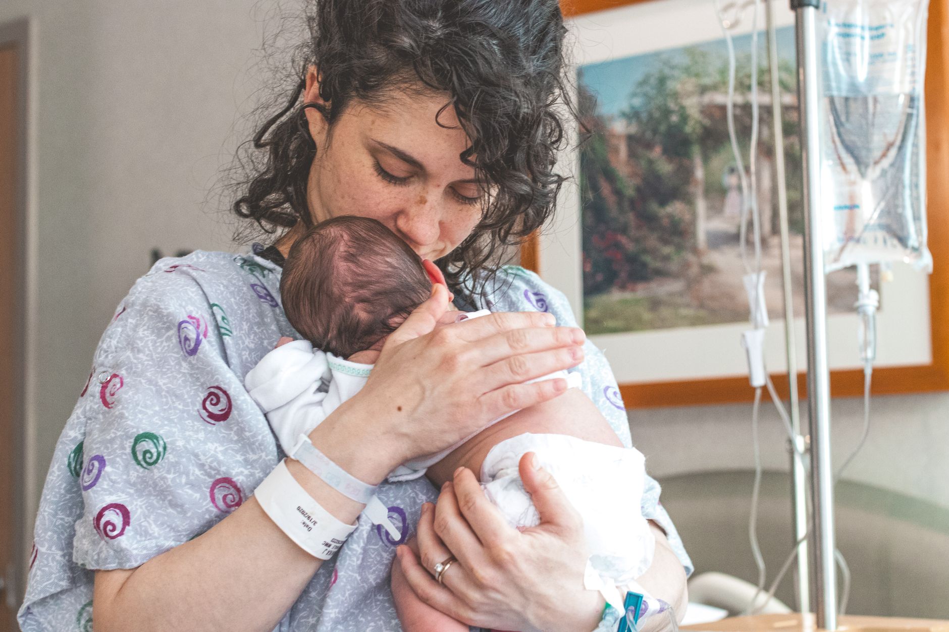 A mother holds her newborn baby close in a hospital room, showing affection.