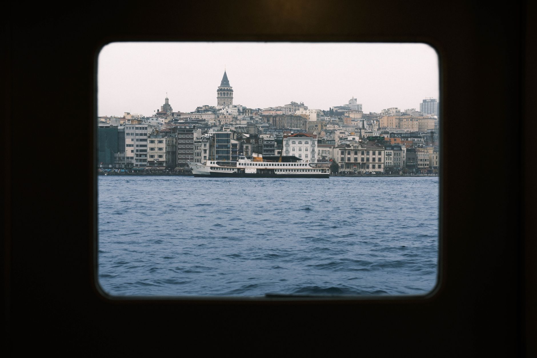 View of Istanbul's skyline from a window, showcasing heritage buildings and a boat on the water.
