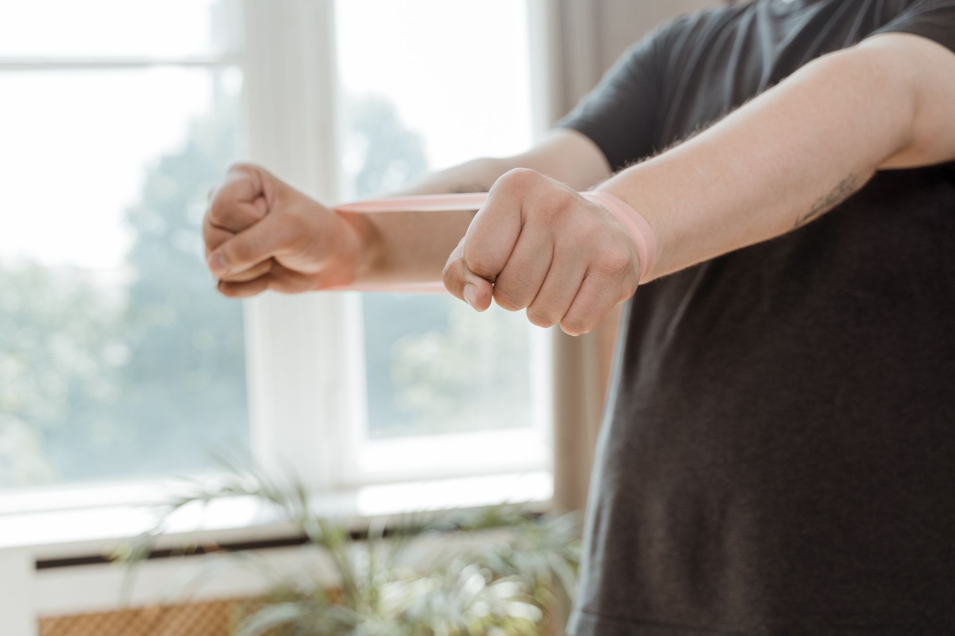 Patient stretching a pink resistance band in a well-lit home setting.