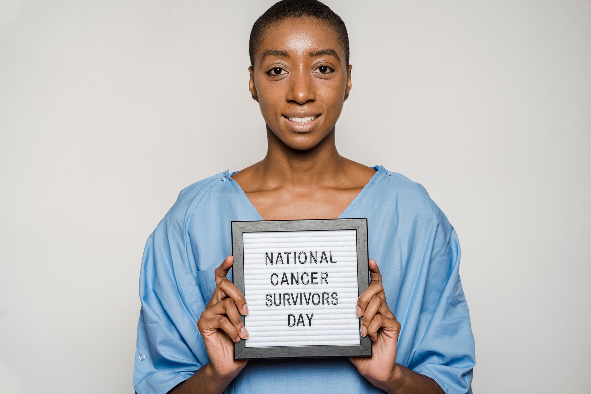 A happy cancer survivor in a blue gown holding a sign for National Cancer Survivors Day.