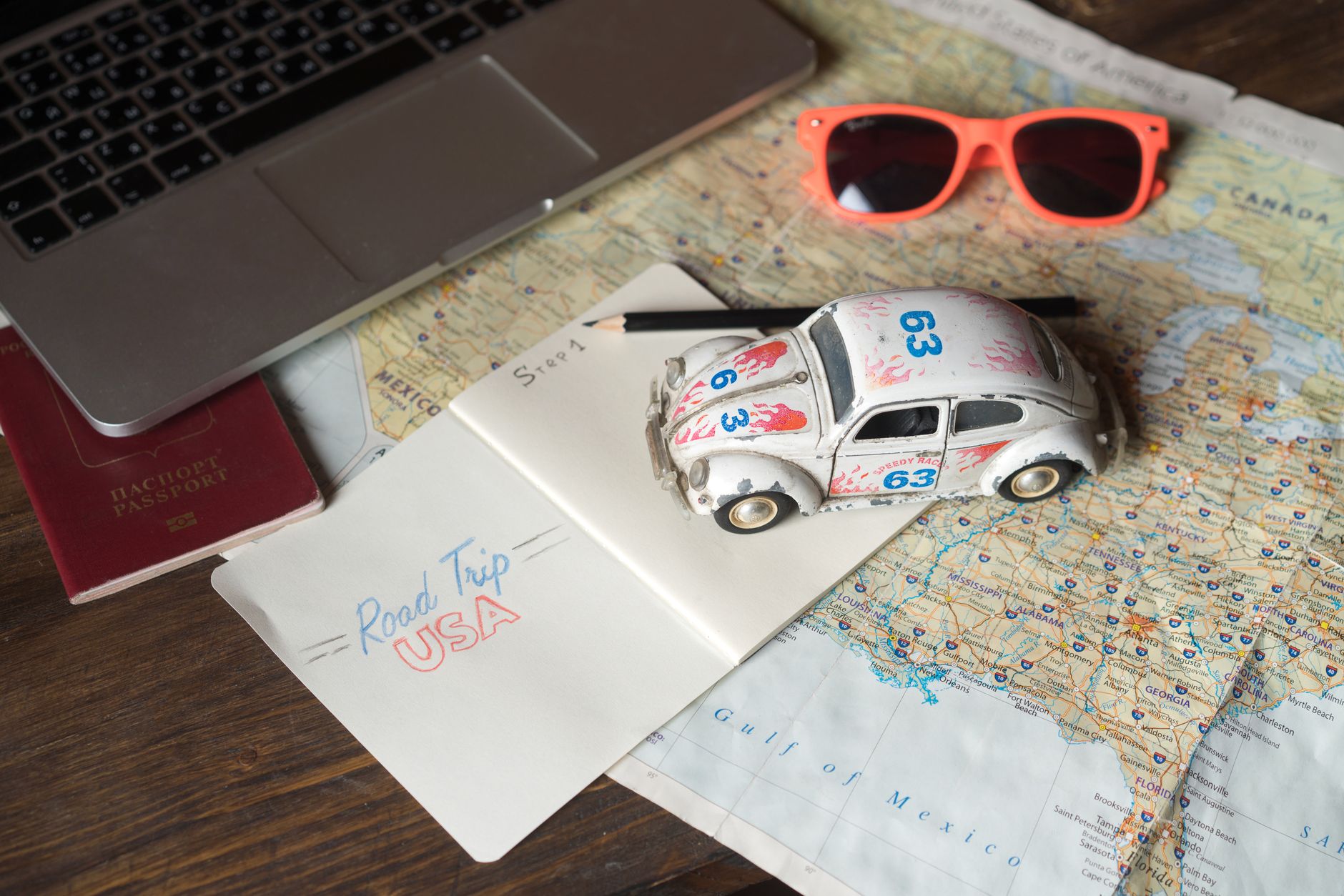 Detailed travel planning for a USA road trip featuring a map, passport, toy car, and sunglasses.