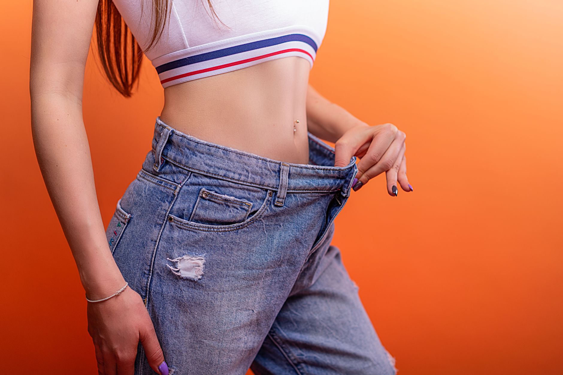 A woman confidently holds her oversized jeans, representing body contouring success.