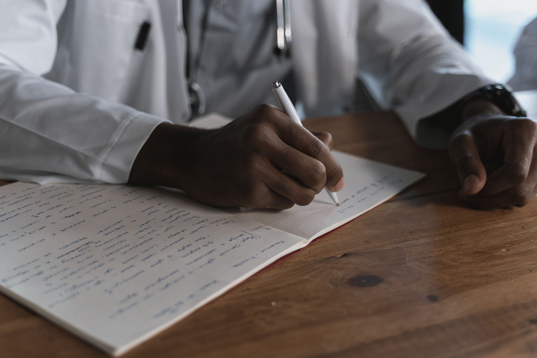 A healthcare professional in a white coat writing notes in a notebook.