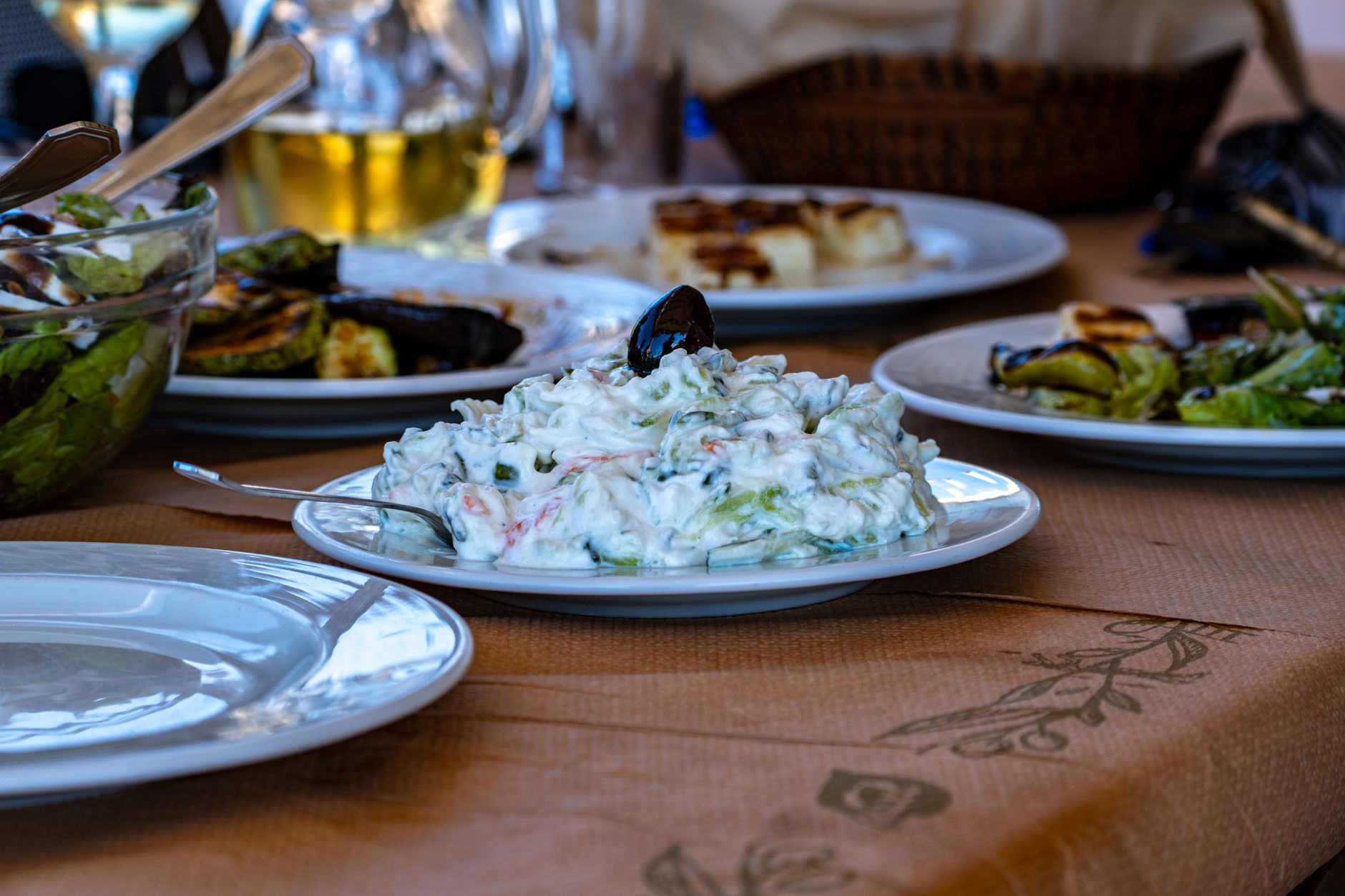 Bir köy restoranında masada salata, ızgara sebzeler ve kremalı mezeler dahil çeşitli Ege mezeleri.