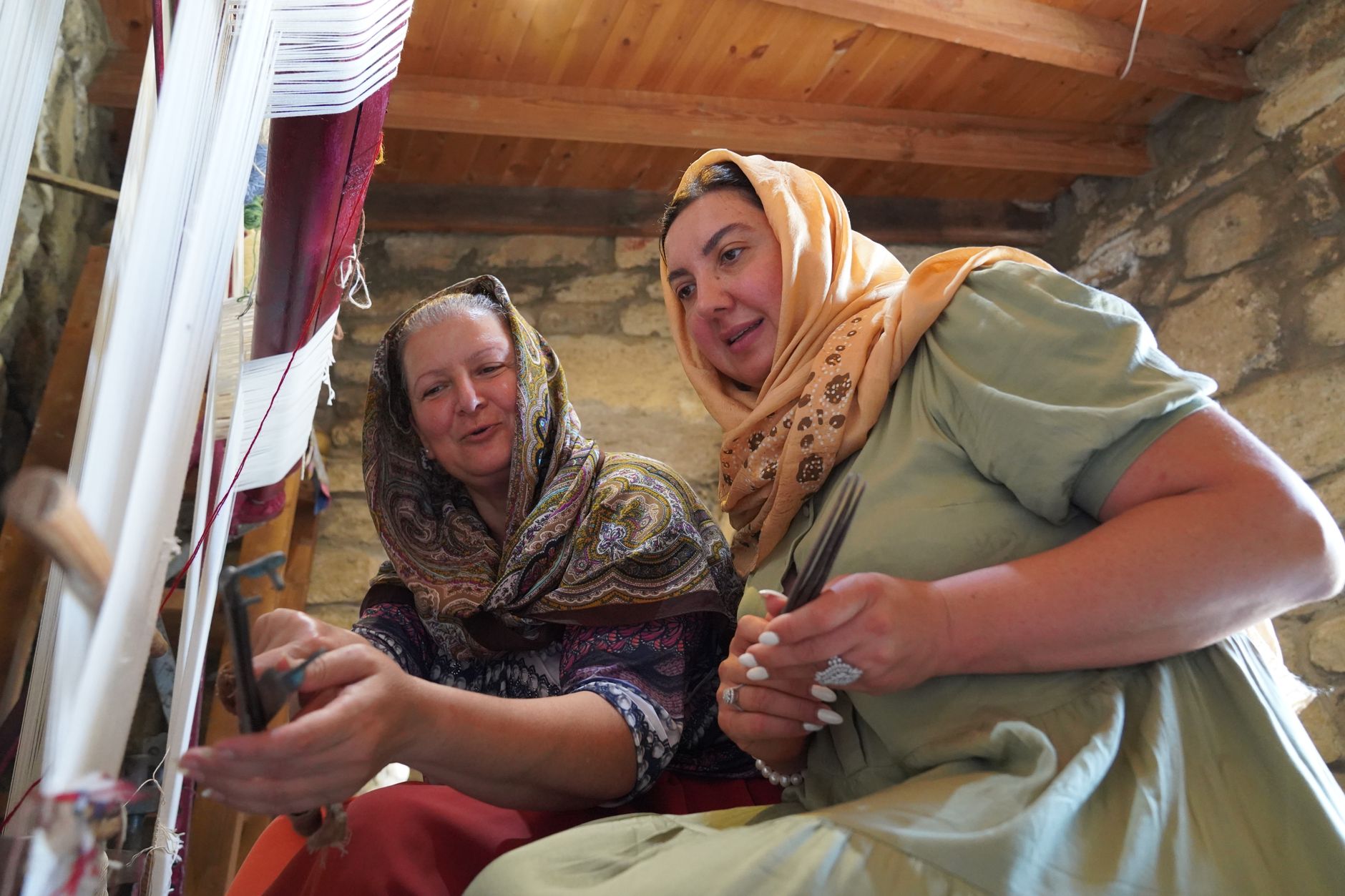 دو زن که در روستایی در منطقه اژه با هم پشت دار قالی سنتی کار می‌کنند.