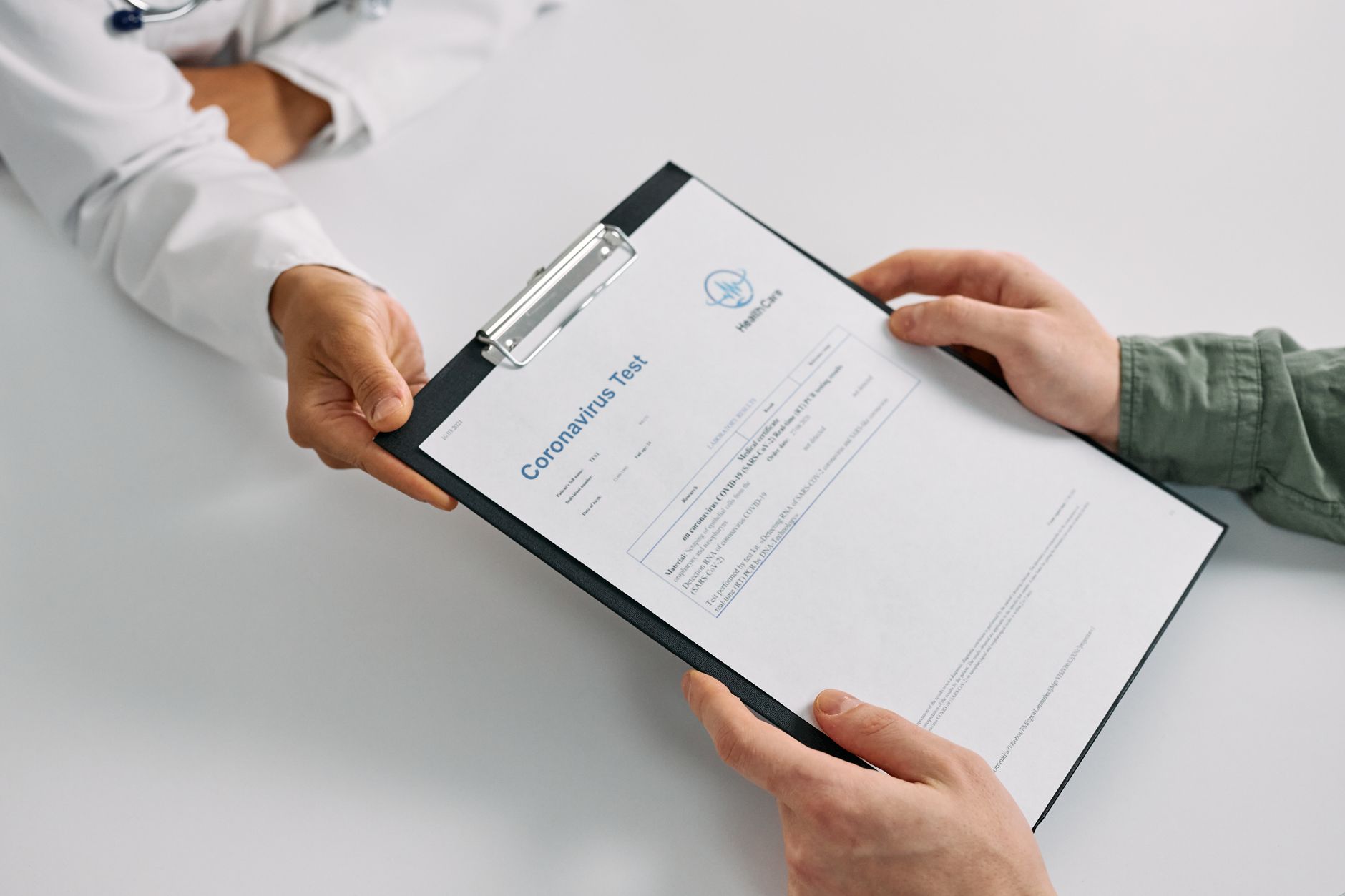 A doctor hands a clipboard with coronavirus test results to a patient in a medical setting.