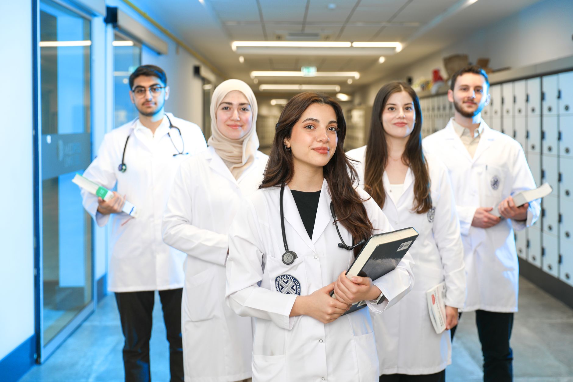 Group of doctors and nurses in white coats, smiling in hospital hallway.