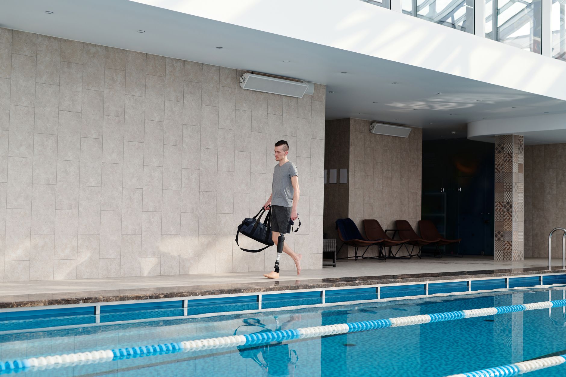 A person carrying a bag walks by a hydrotherapy pool in a rehabilitation center.