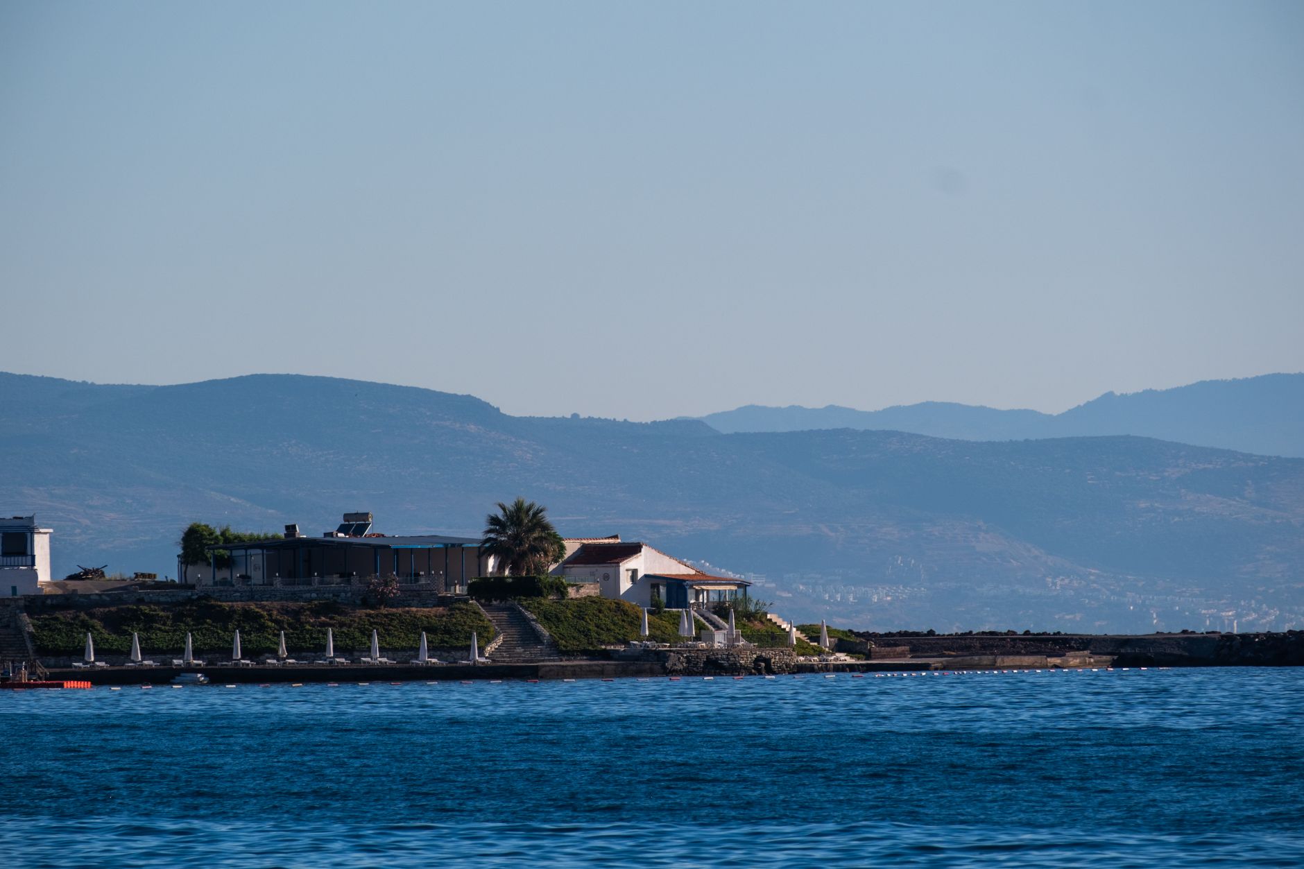 Serene view of Aegean coastline near Cesme, featuring homes and mountains.