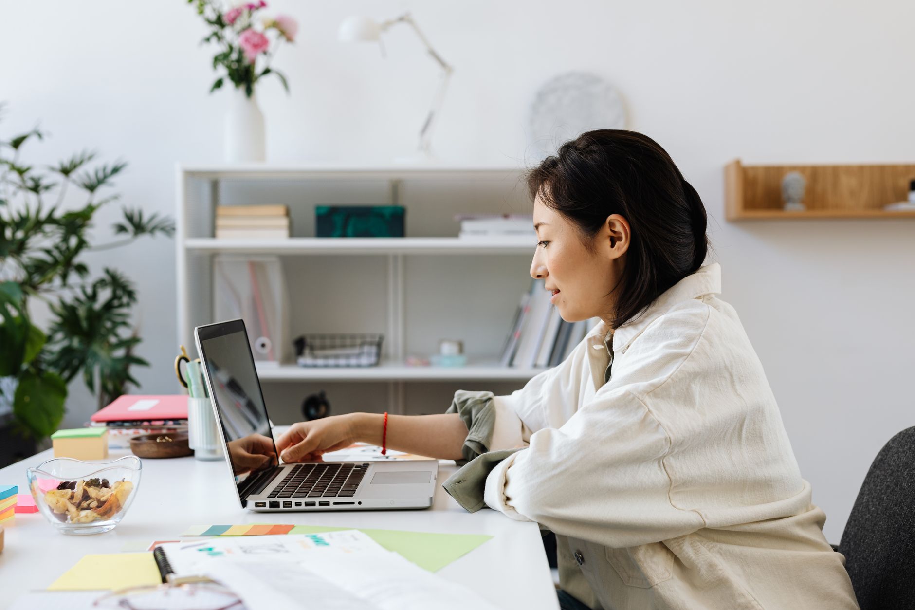 A woman working on a laptop at a clean home office desk with plants.