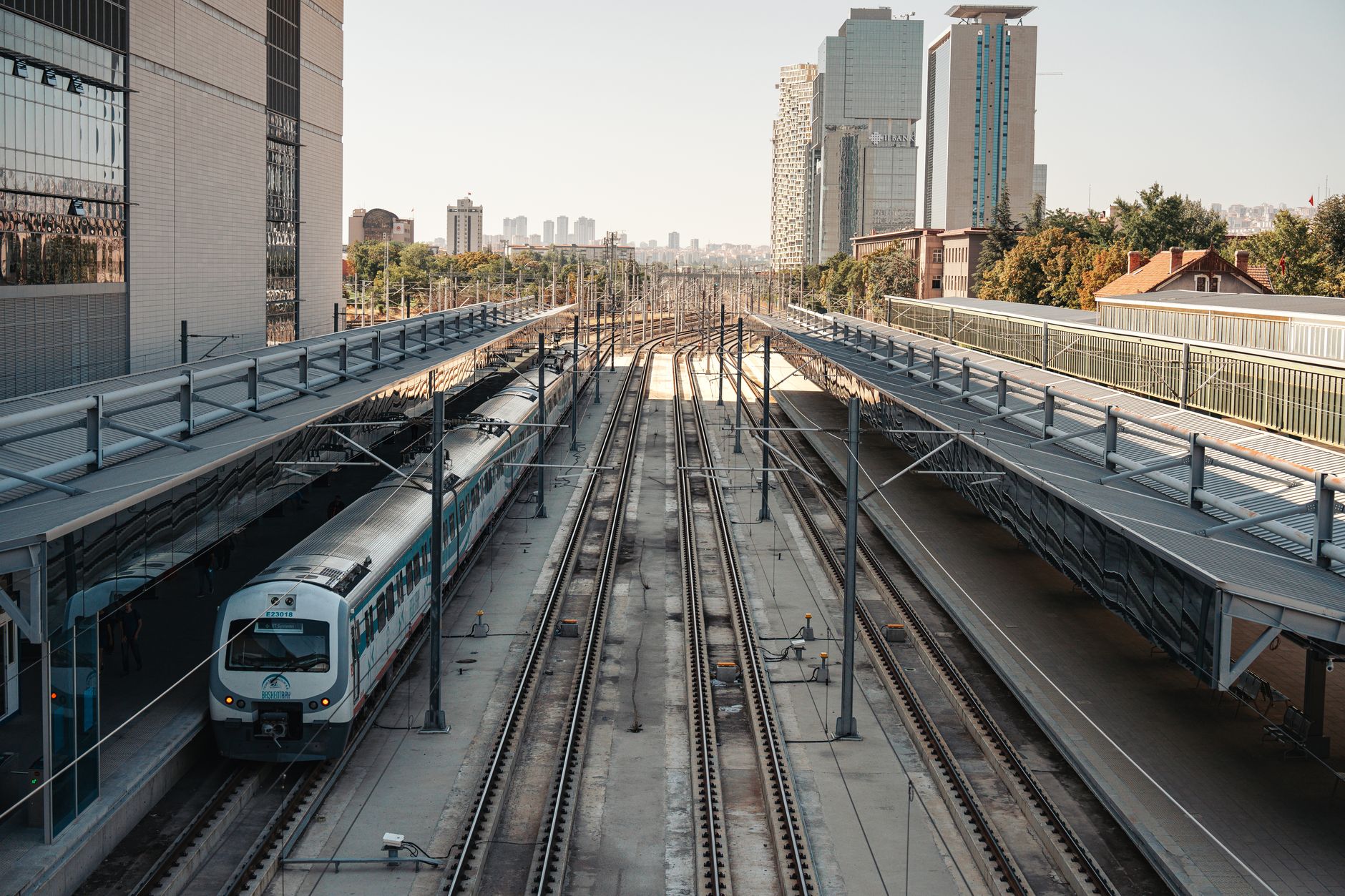 A sleek high-speed train at Ankara station, surrounded by urban architecture and railway tracks.