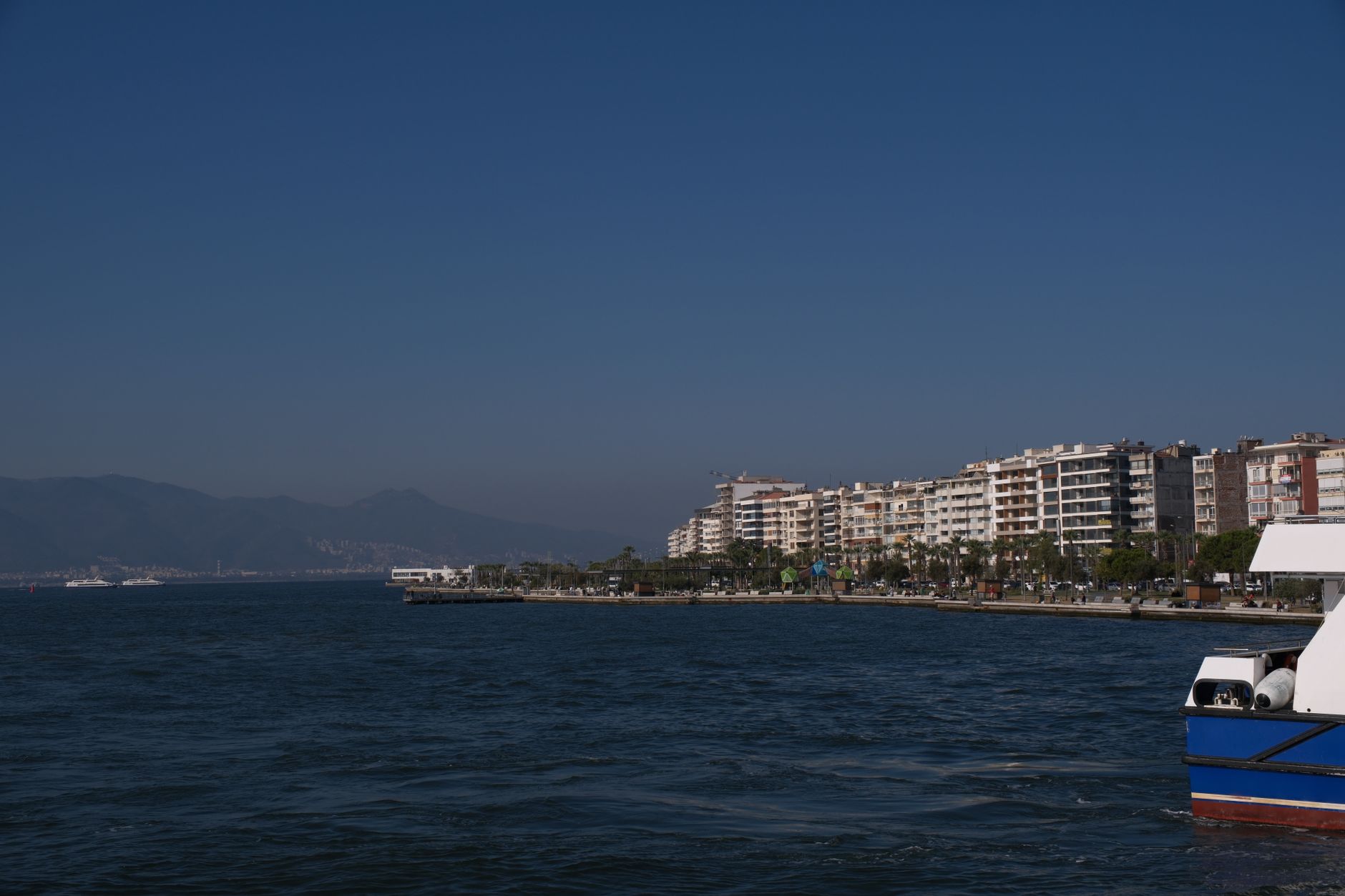 A picturesque view of the coastline of Izmir, Türkiye, featuring modern buildings and vibrant water under a clear blue sky.