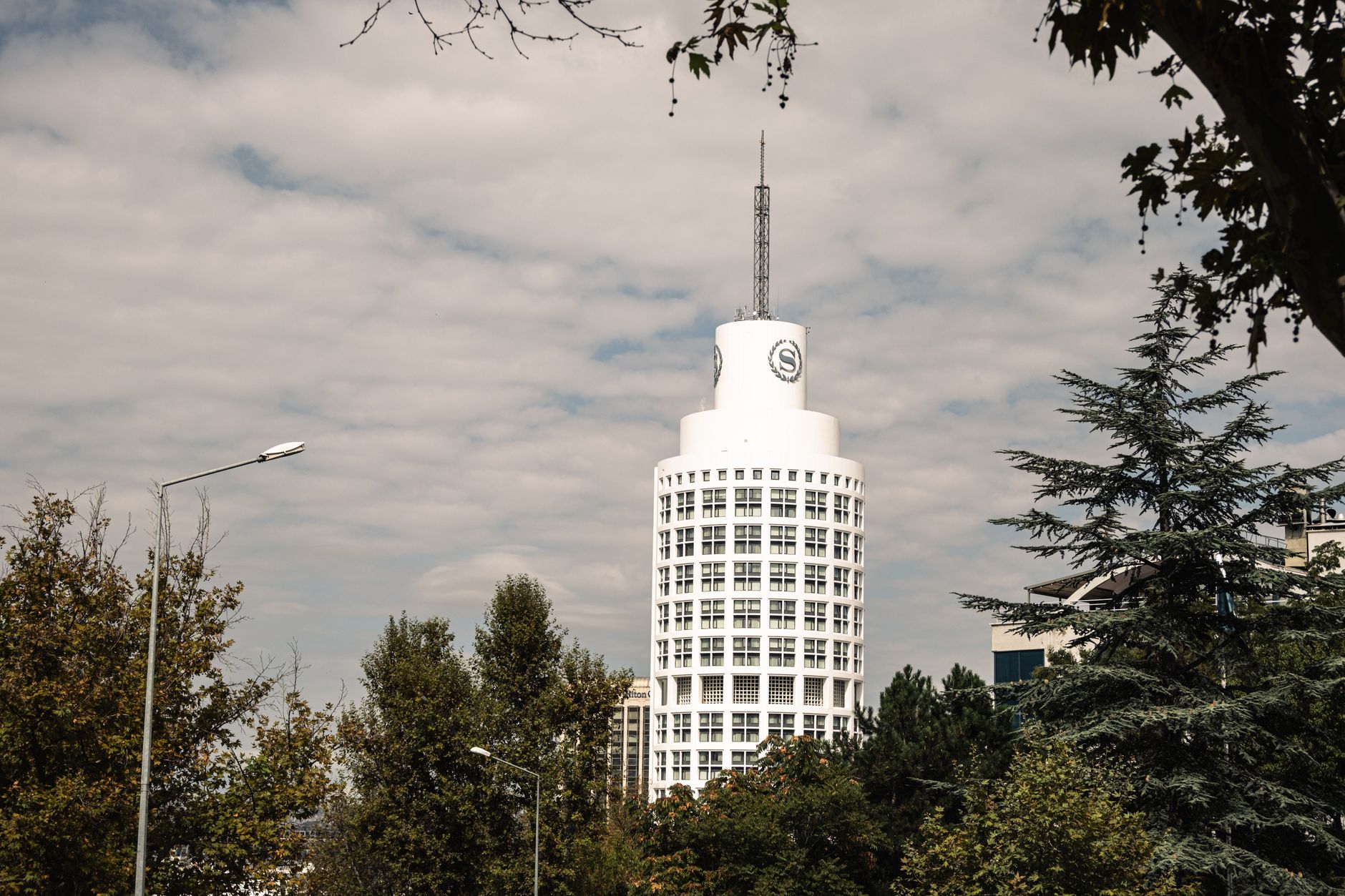 View of a modern hospital building in Ankara, surrounded by trees and under a cloudy sky.
