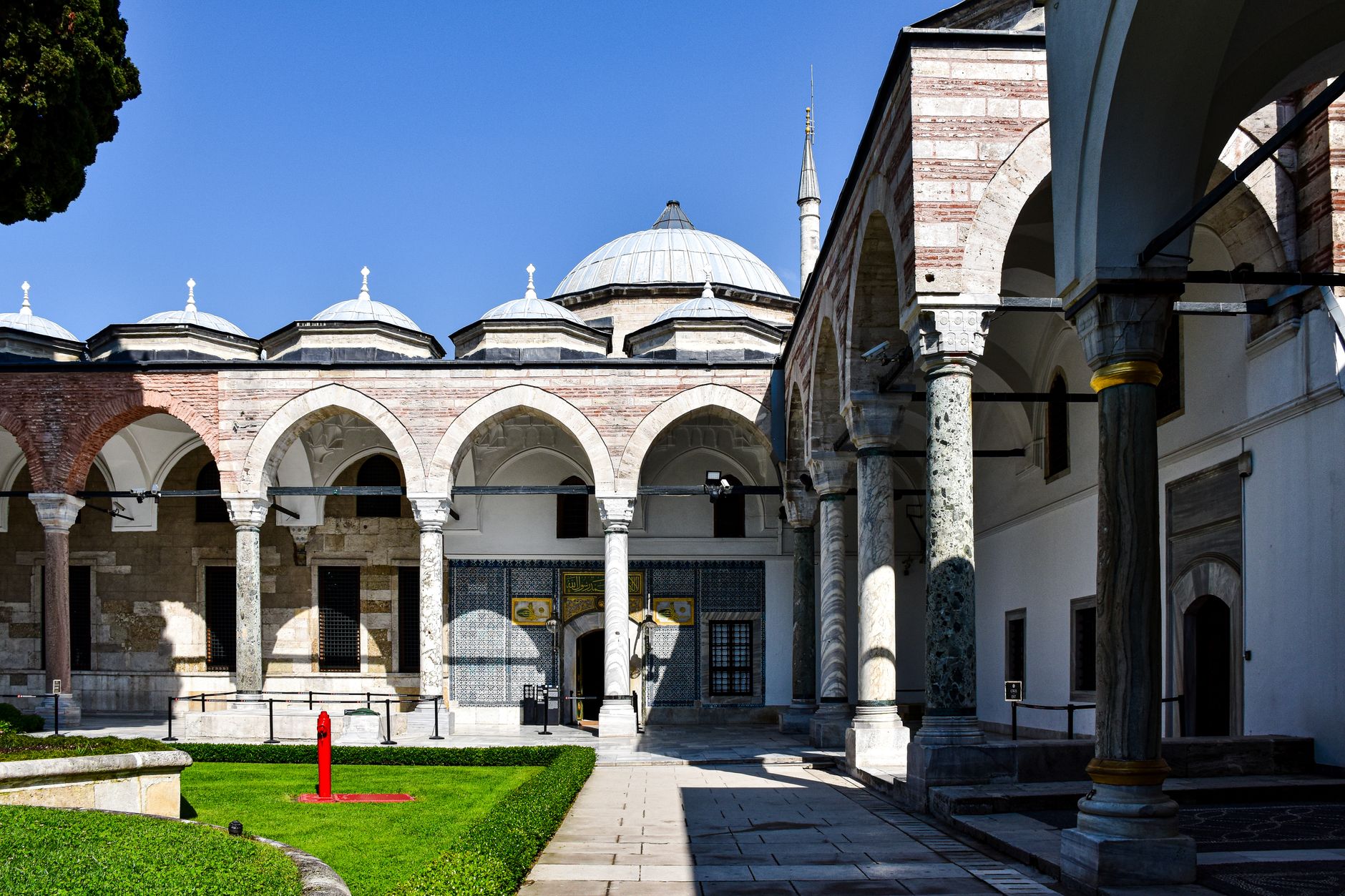 Courtyard of the Great Palace in Istanbul featuring arches, domes, and a green lawn.