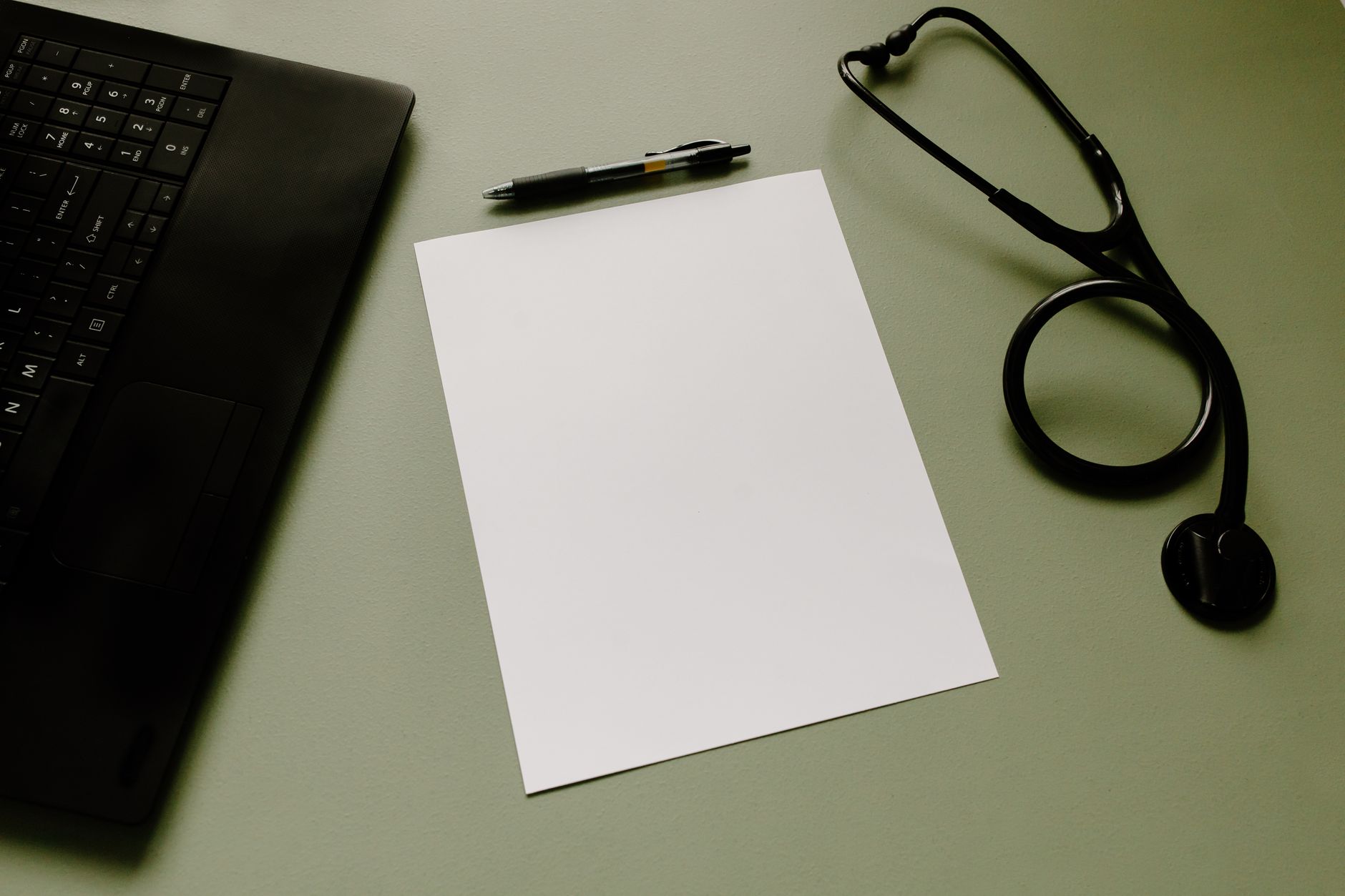 A medical workspace featuring a laptop, stethoscope, and blank paper for patient scans and reports.