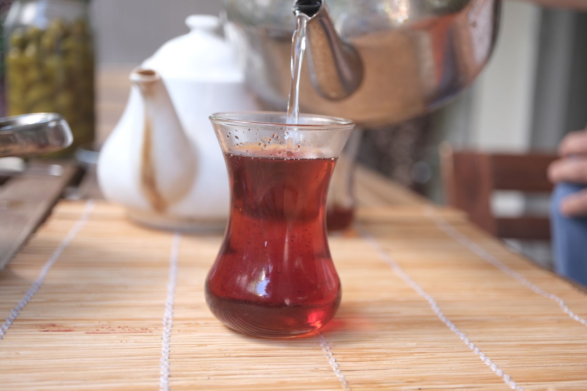 كوب من الشاي التركي المسكوب طازجًا، مع إبريق شاي في الخلفية في حديقة شاي على جانب الطريق.