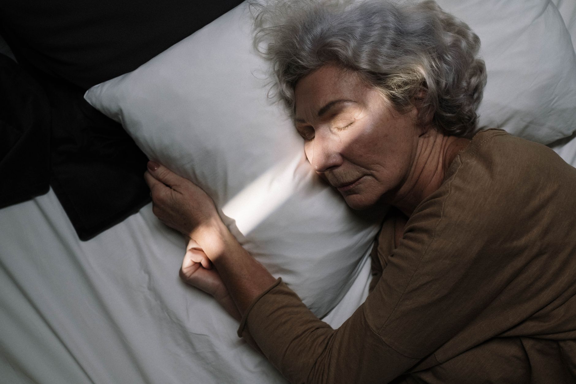 An elderly woman rests on a pillow in a sleep study lab, bathed in soft light.
