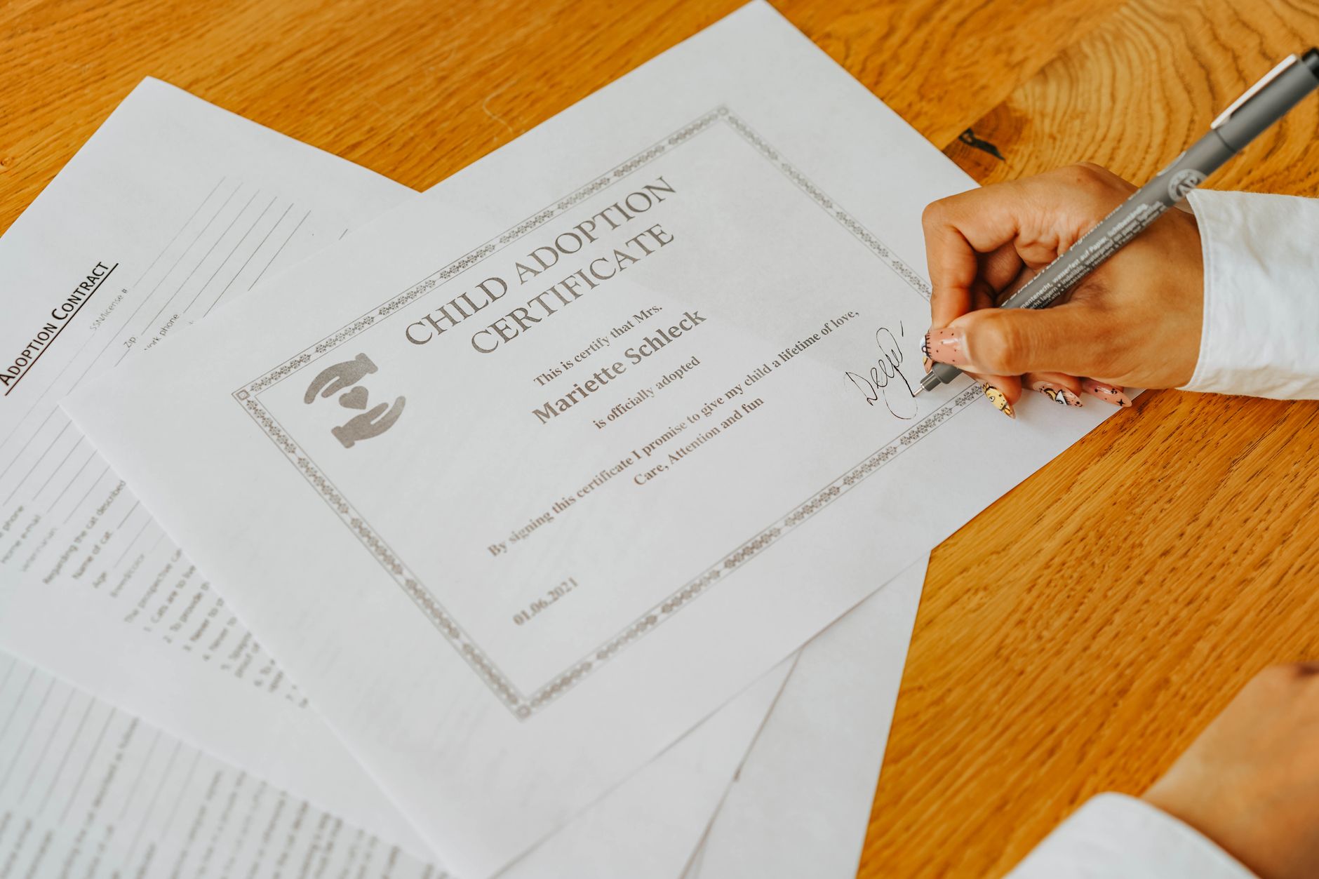 Close-up of a child adoption certificate being signed with a pen on a wooden desk.