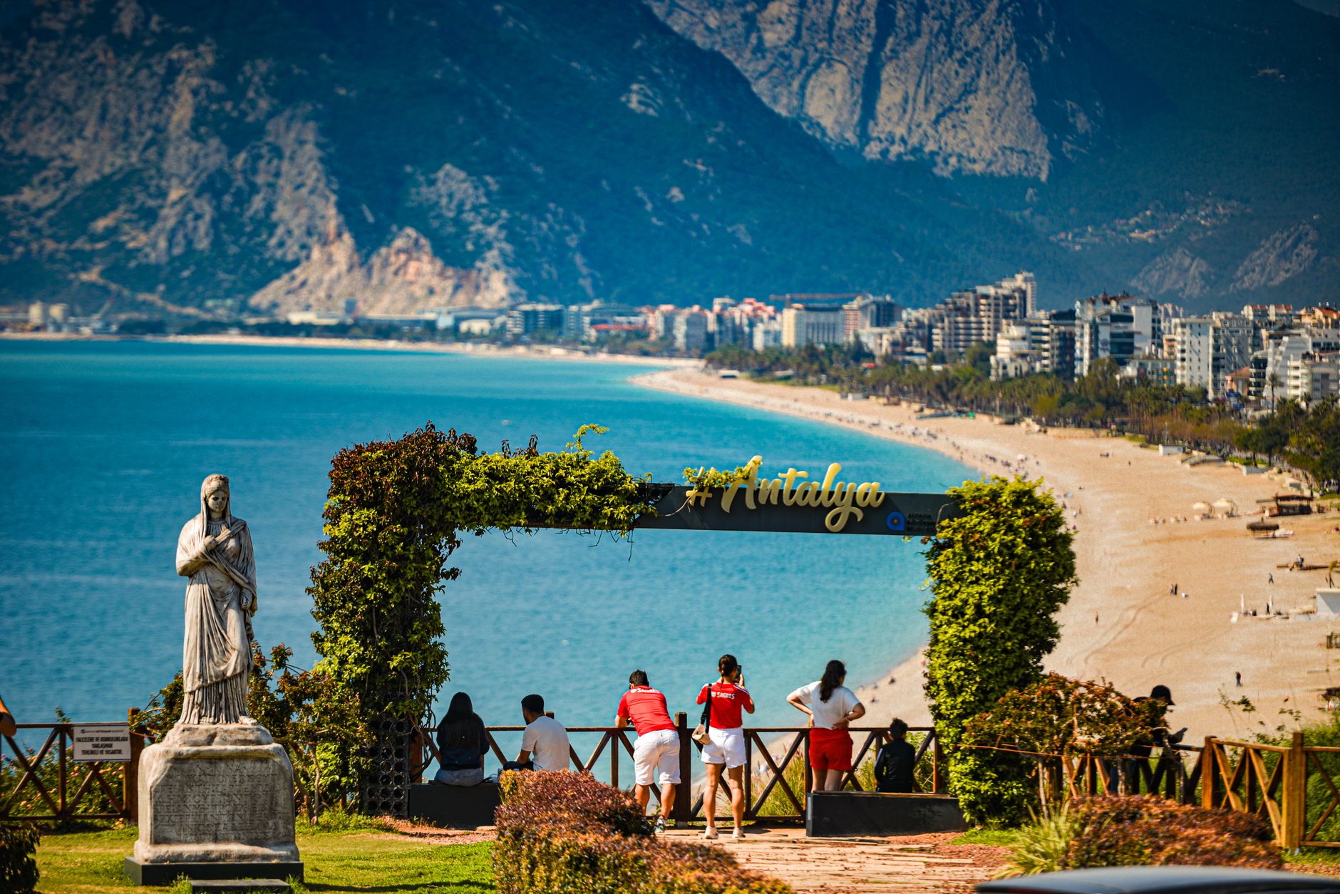 Antalya'da plaj, dağlar ve manzaranın keyfini çıkaran ziyaretçileri gösteren bir bakış noktası.
