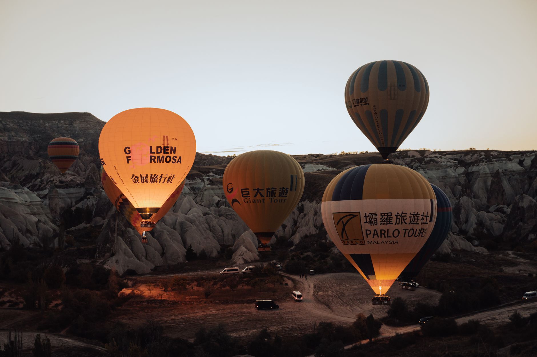 Colorful hot air balloons illuminate the sky over Cappadocia's unique landscape at dusk.