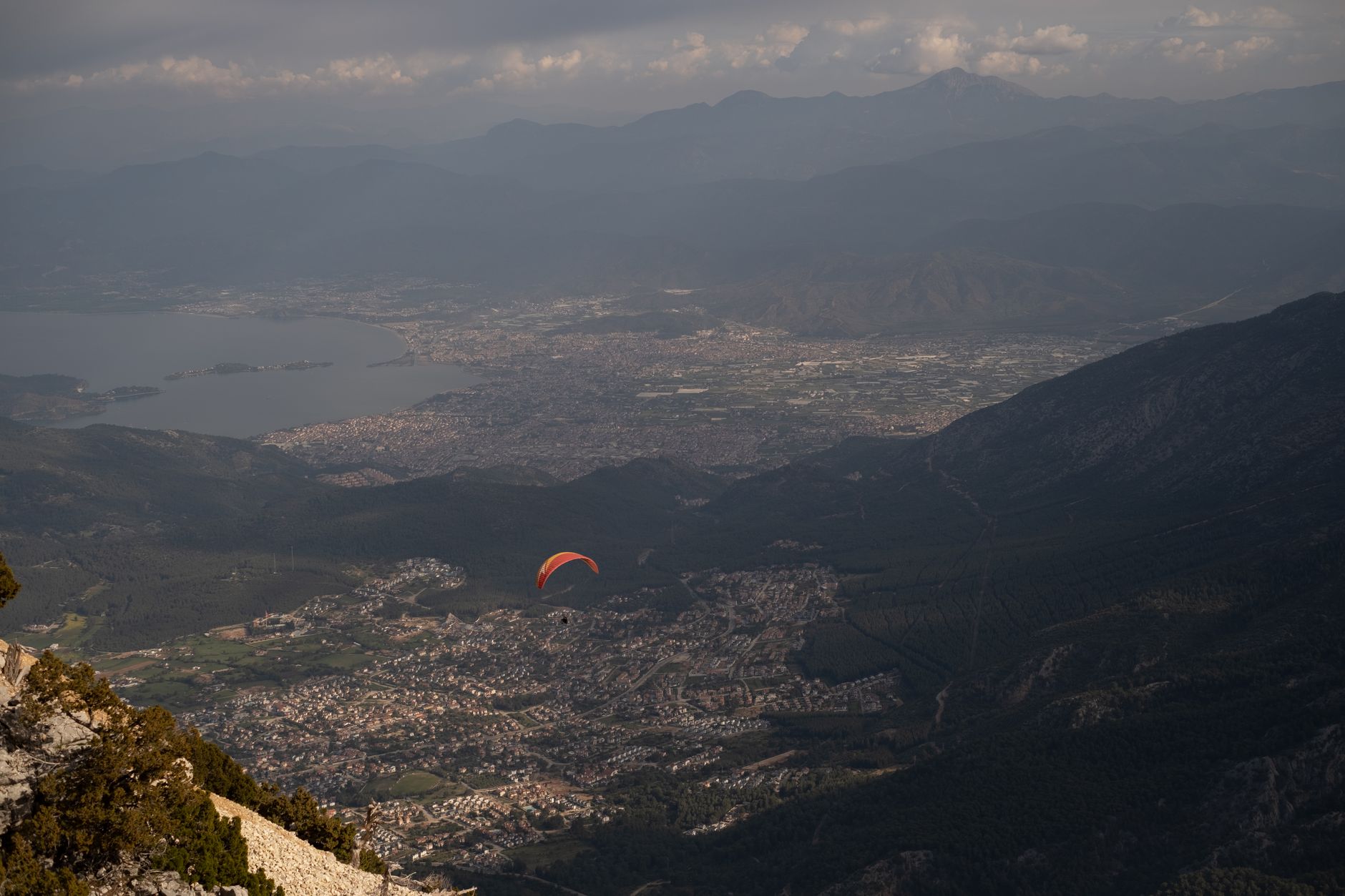 A vibrant paraglider floats above the Ölüdeniz Blue Lagoon and mountainous landscape.