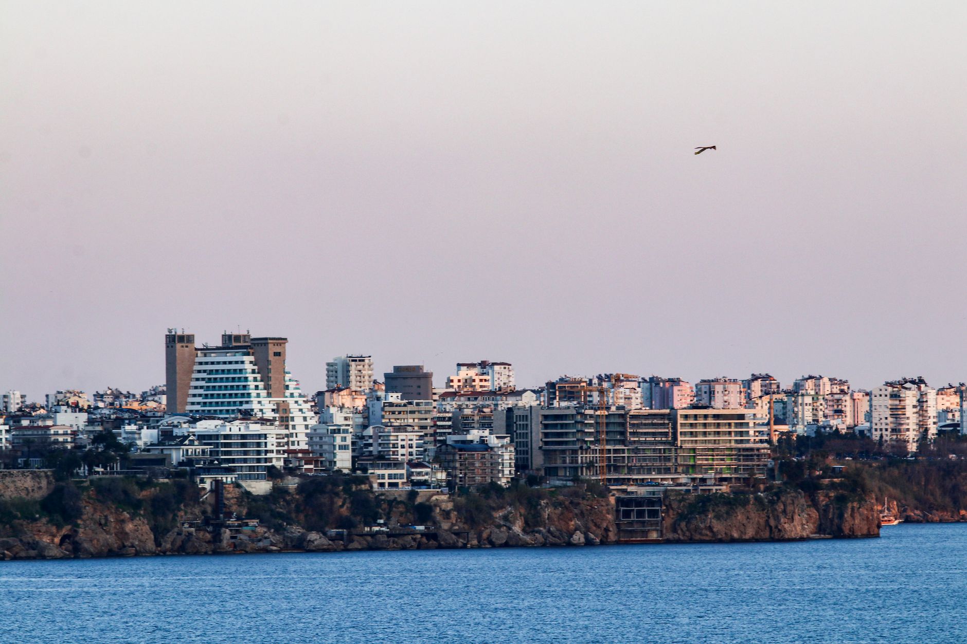 A scenic view of Antalya's cliffs during sunset, with modern buildings overlooking the Mediterranean Sea.