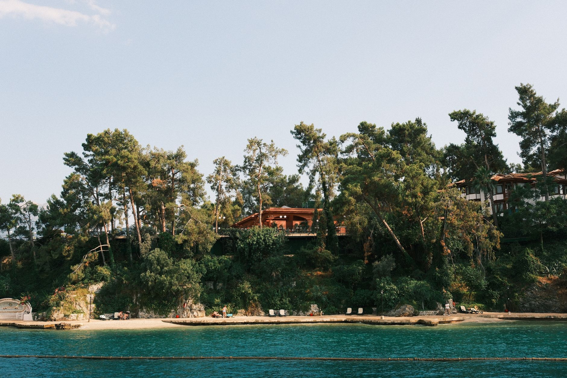A scenic view of an eco-lodge nestled among trees by the turquoise waters of Türkiye.