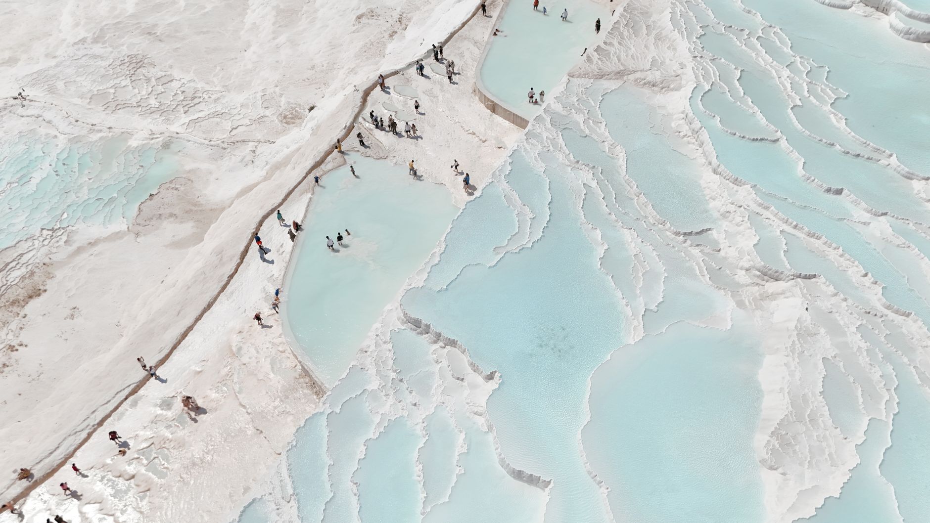 Aerial view of Pamukkale's thermal pools with people enjoying the blue waters.