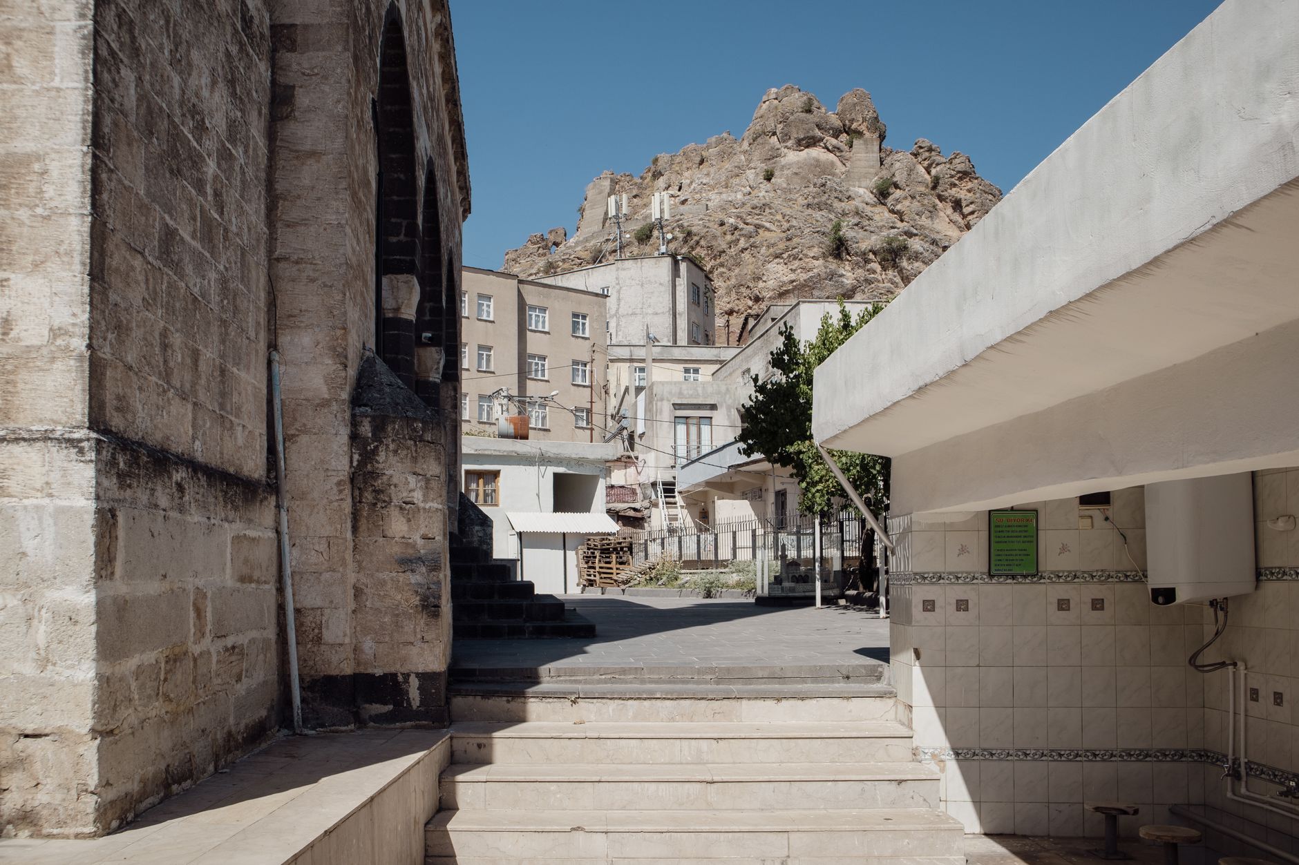Serene view of Çermik's thermal baths, surrounded by plain buildings and a rocky hillside.